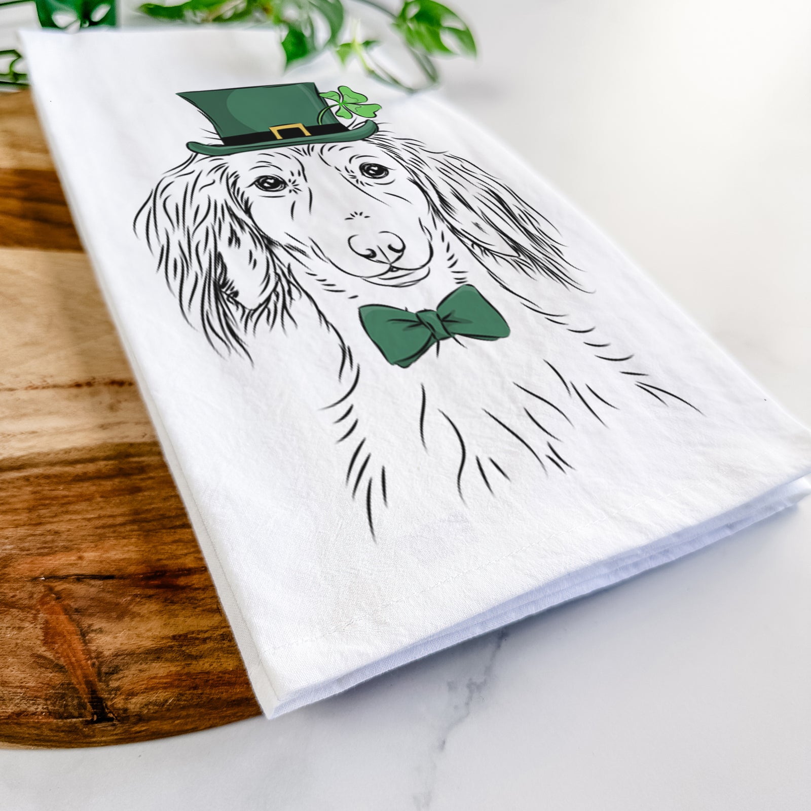 Hand-drawn sketch of Roux the Long Haired Dachshund wearing a St. Patrick's Day leprechaun hat and bow tie on a tea towel