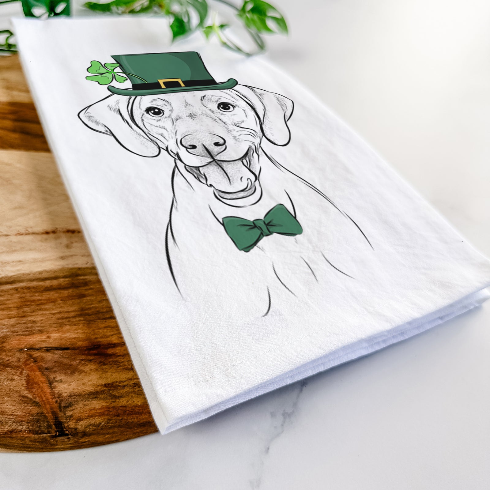 Hand-drawn sketch of Ruby the Vizsla wearing a St. Patrick's Day leprechaun hat and bow tie on a tea towel