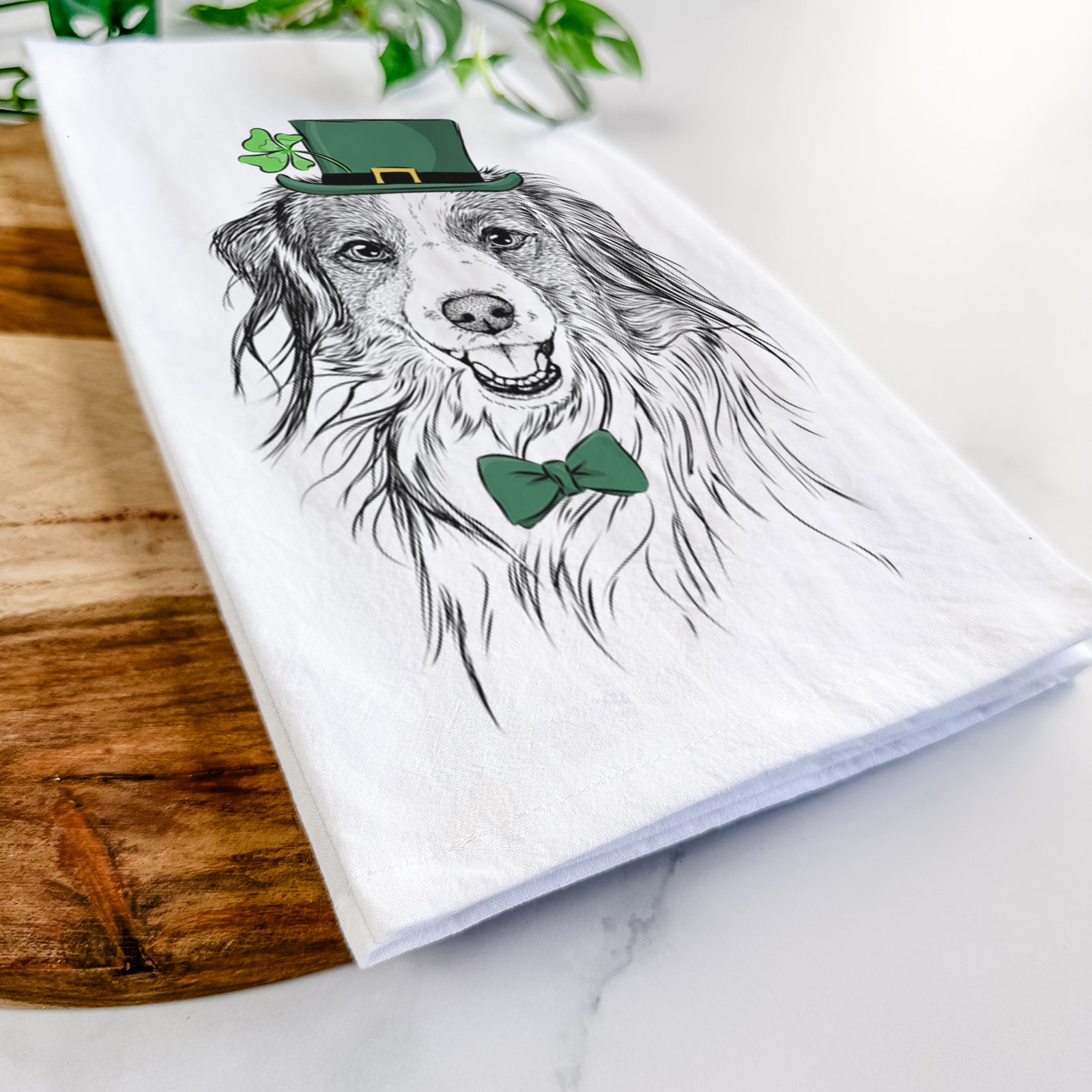 Hand-drawn sketch of Rutger the Nederlandse Kooikerhondje wearing a St. Patrick's Day leprechaun hat and bow tie on a tea towel