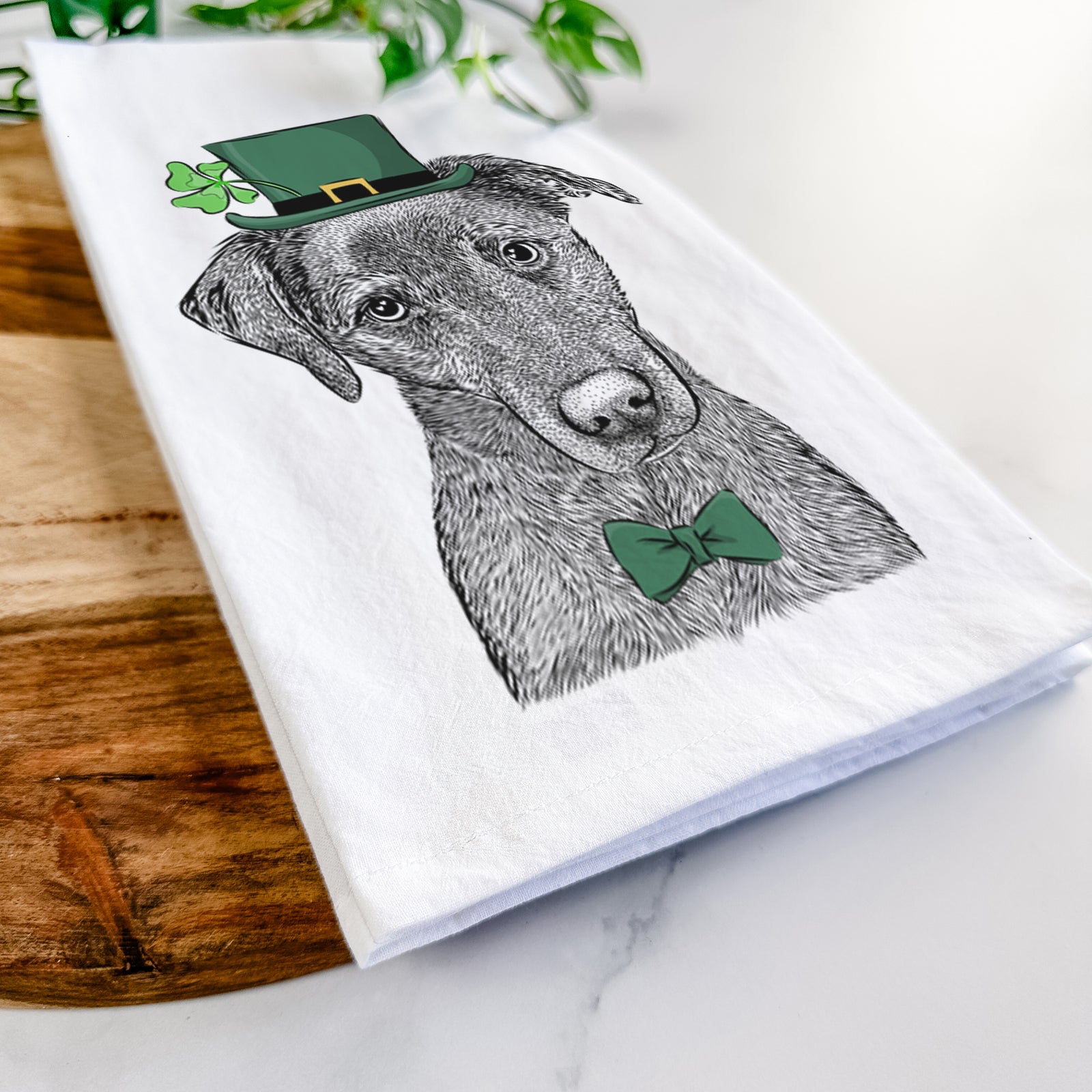 Hand-drawn sketch of Sadie the Whipador wearing a St. Patrick's Day leprechaun hat and bow tie on a tea towel
