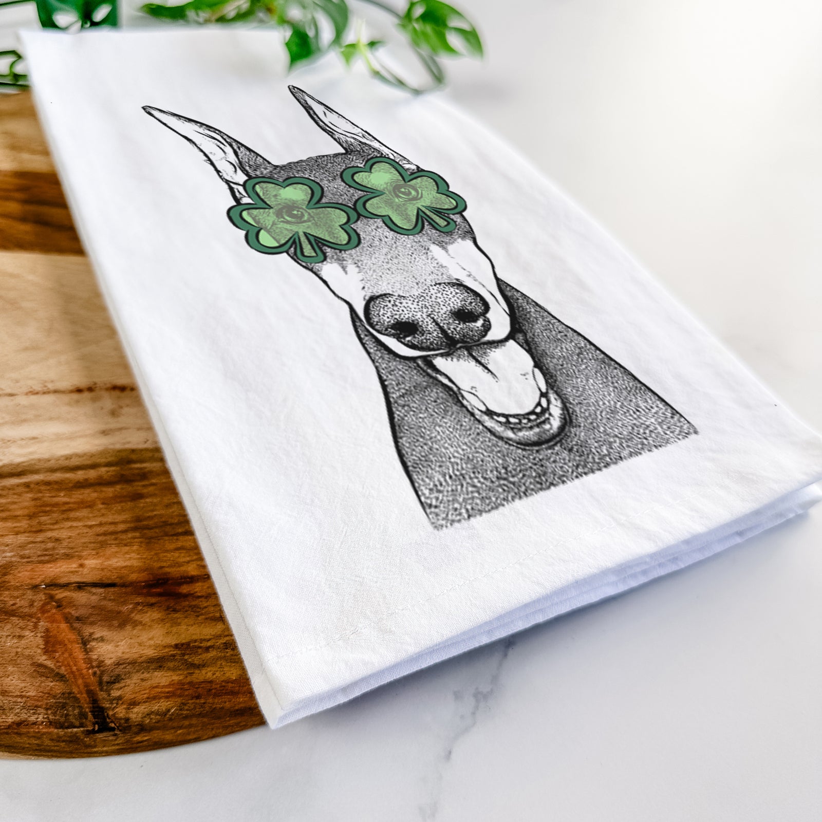 Hand-drawn sketch of Sir Duke the Doberman Pinscher wearing a St. Patrick's Day leprechaun hat and bow tie on a tea towel