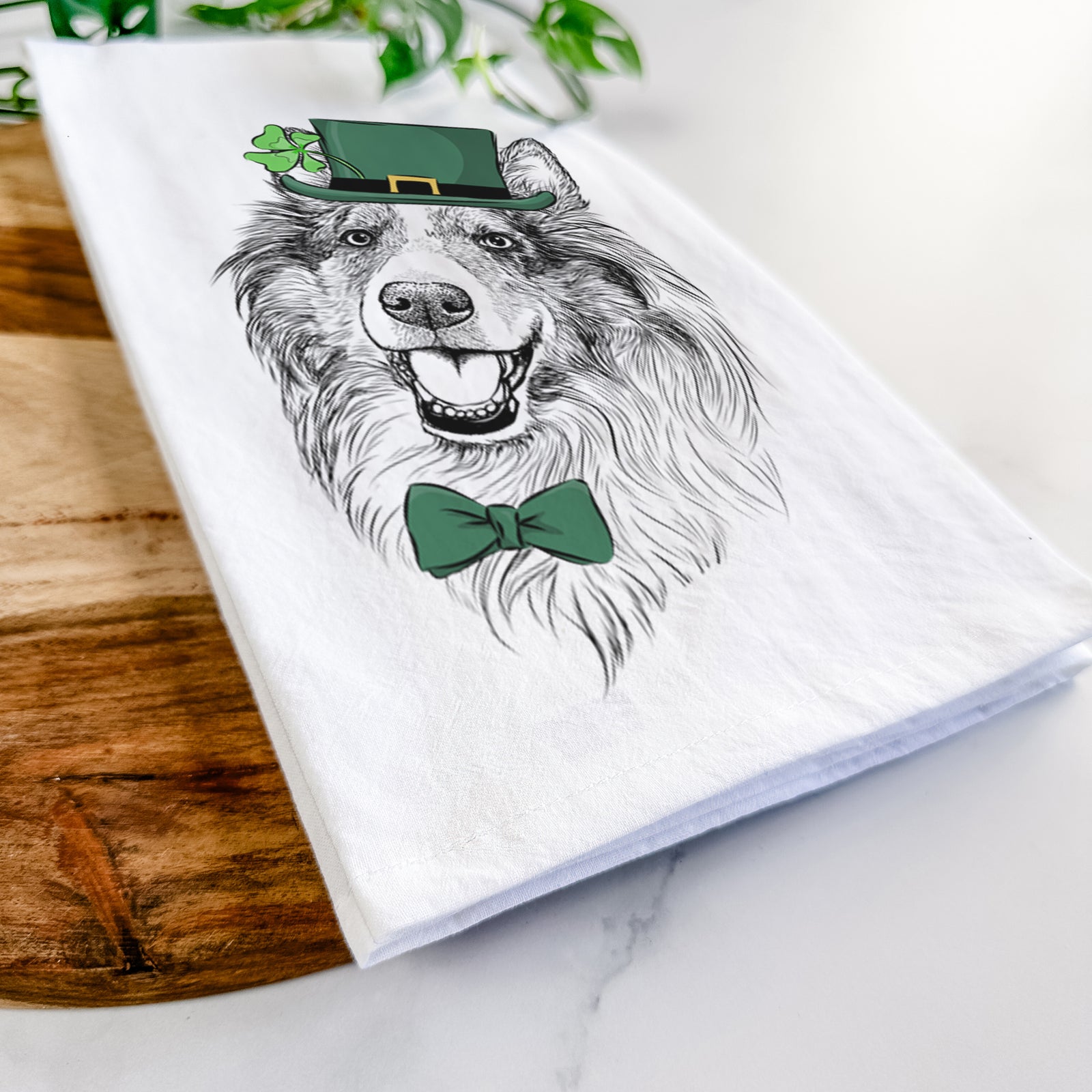 Hand-drawn sketch of Skylar the Shetland Sheepdog wearing a St. Patrick's Day leprechaun hat and bow tie on a tea towel