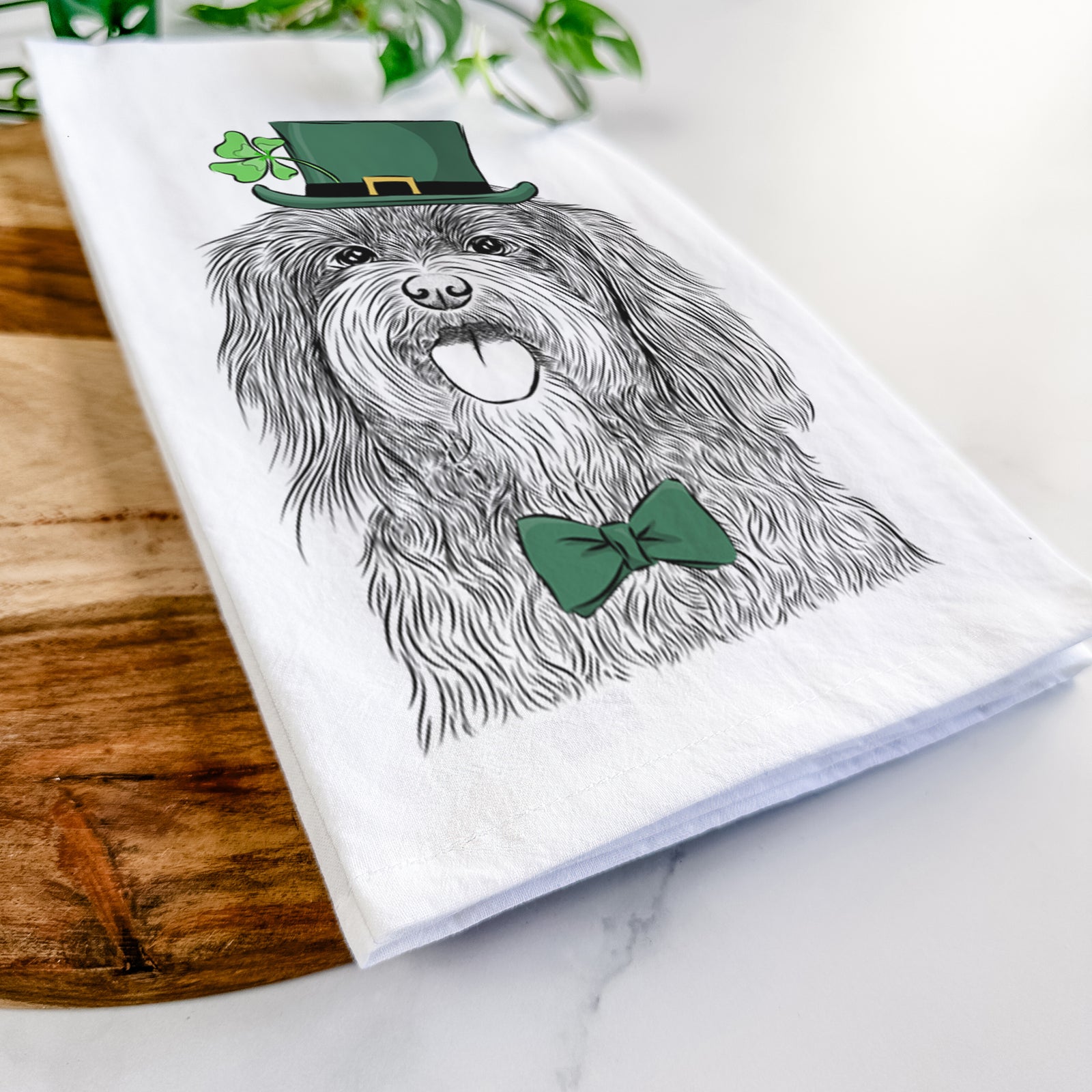 Hand-drawn sketch of Sophie the Havanese wearing a St. Patrick's Day leprechaun hat and bow tie on a tea towel