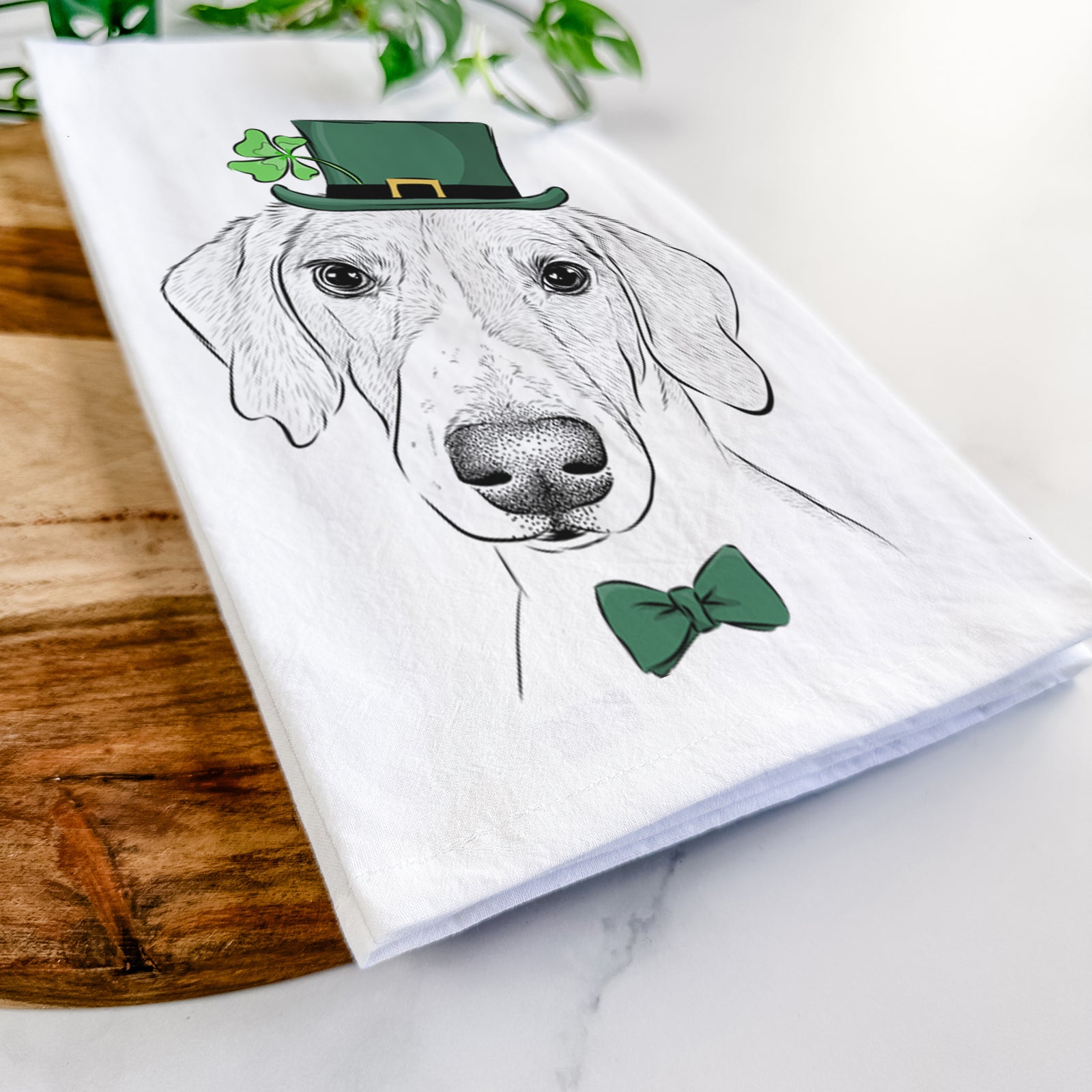 Hand-drawn sketch of Stanley the Foxhound wearing a St. Patrick's Day leprechaun hat and bow tie on a tea towel