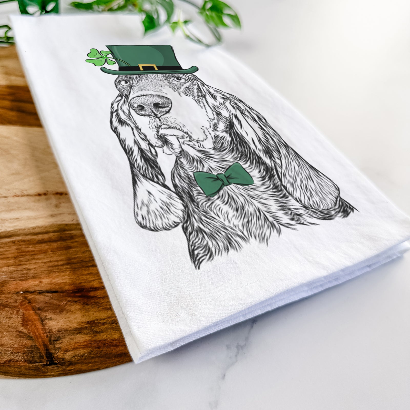 Hand-drawn sketch of Stu the Black and Tan Coonhound wearing a St. Patrick's Day leprechaun hat and bow tie on a tea towel