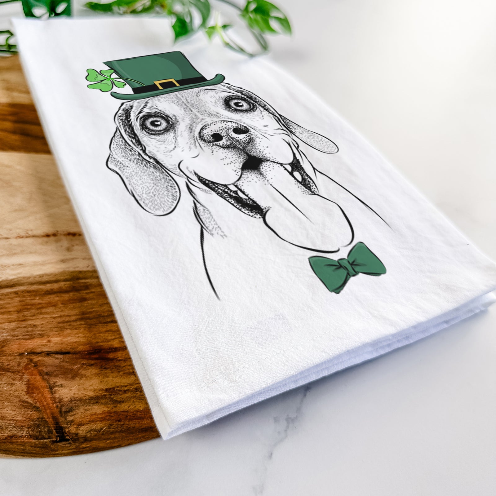 Hand-drawn sketch of Sunny the Beagle wearing a St. Patrick's Day leprechaun hat and bow tie on a tea towel