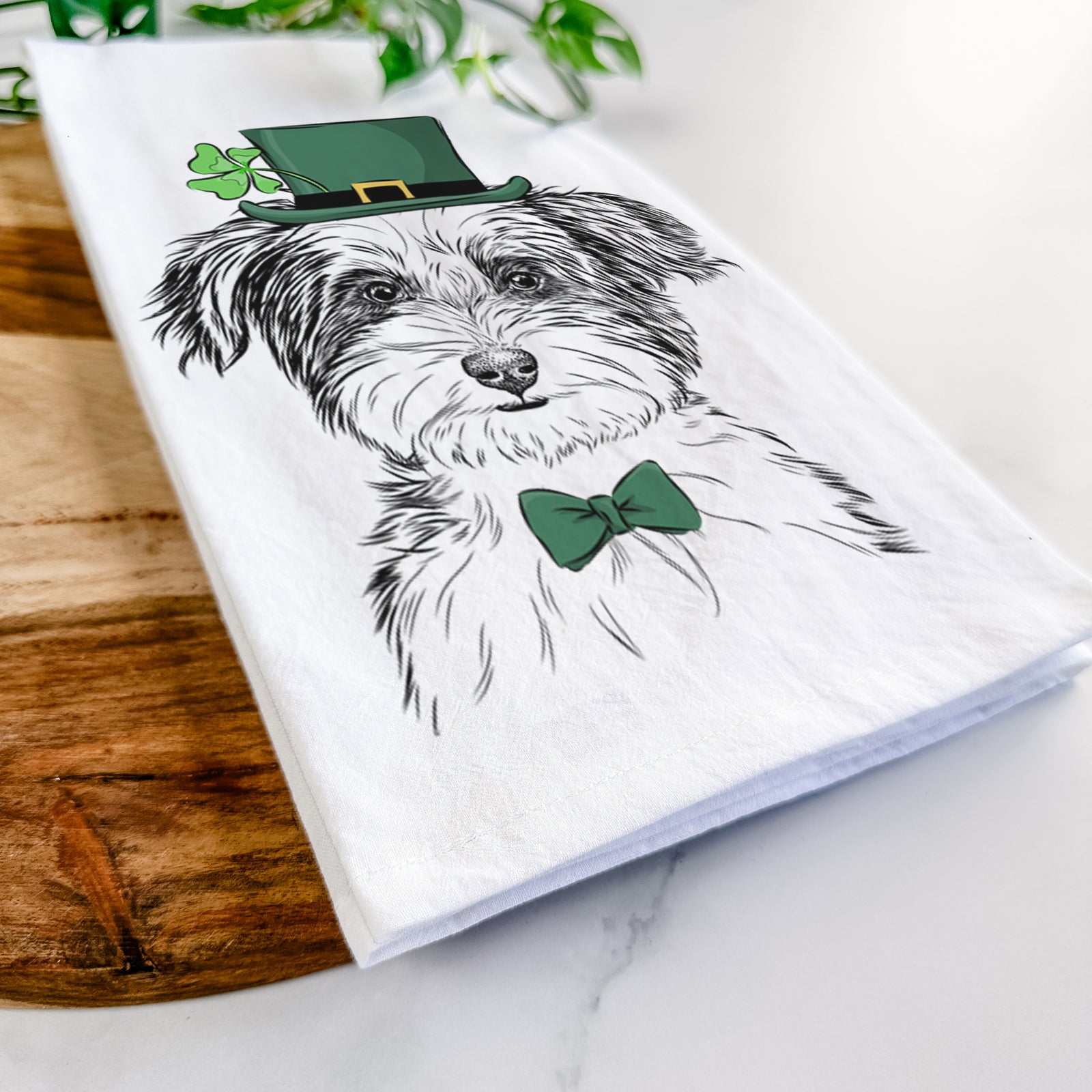 Hand-drawn sketch of Teddy the Havanese wearing a St. Patrick's Day leprechaun hat and bow tie on a tea towel