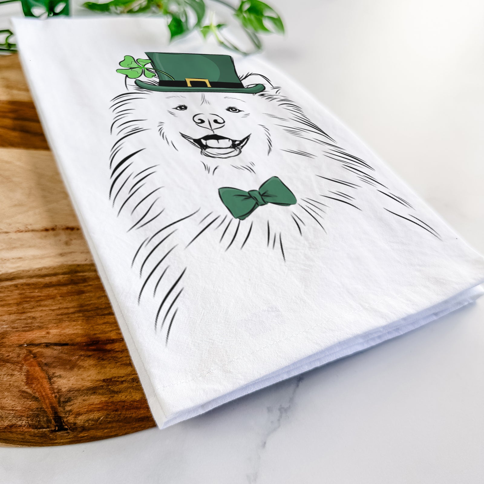 Hand-drawn sketch of Tillie the Samoyed wearing a St. Patrick's Day leprechaun hat and bow tie on a tea towel