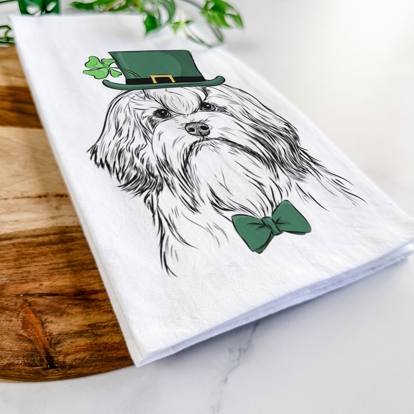 Hand-drawn sketch of Tootsie the Lowchen wearing a St. Patrick's Day leprechaun hat and bow tie on a tea towel