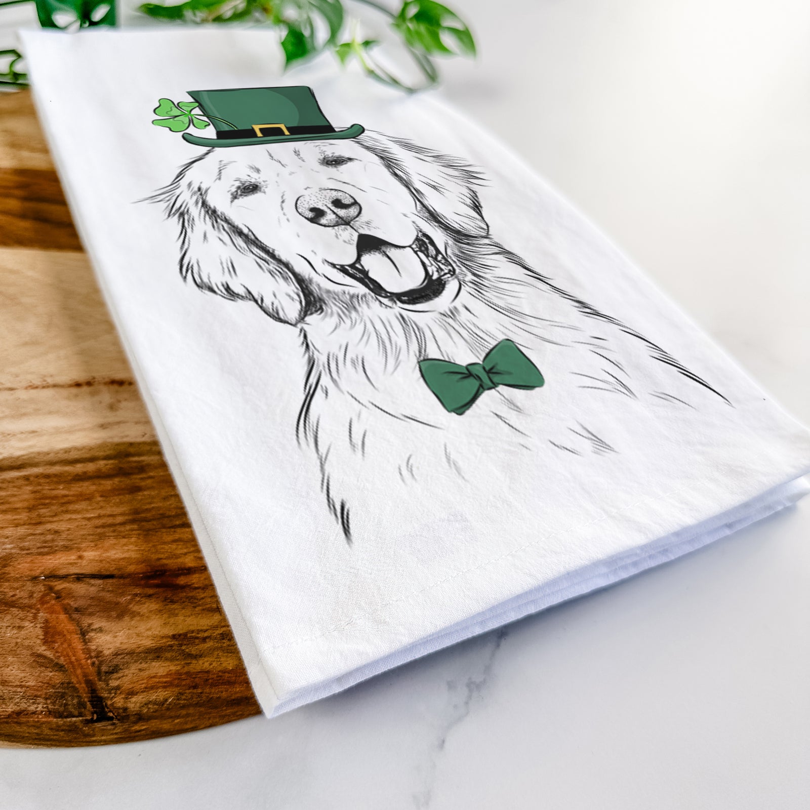 Hand-drawn sketch of Wallace the Golden Retriever wearing a St. Patrick's Day leprechaun hat and bow tie on a tea towel