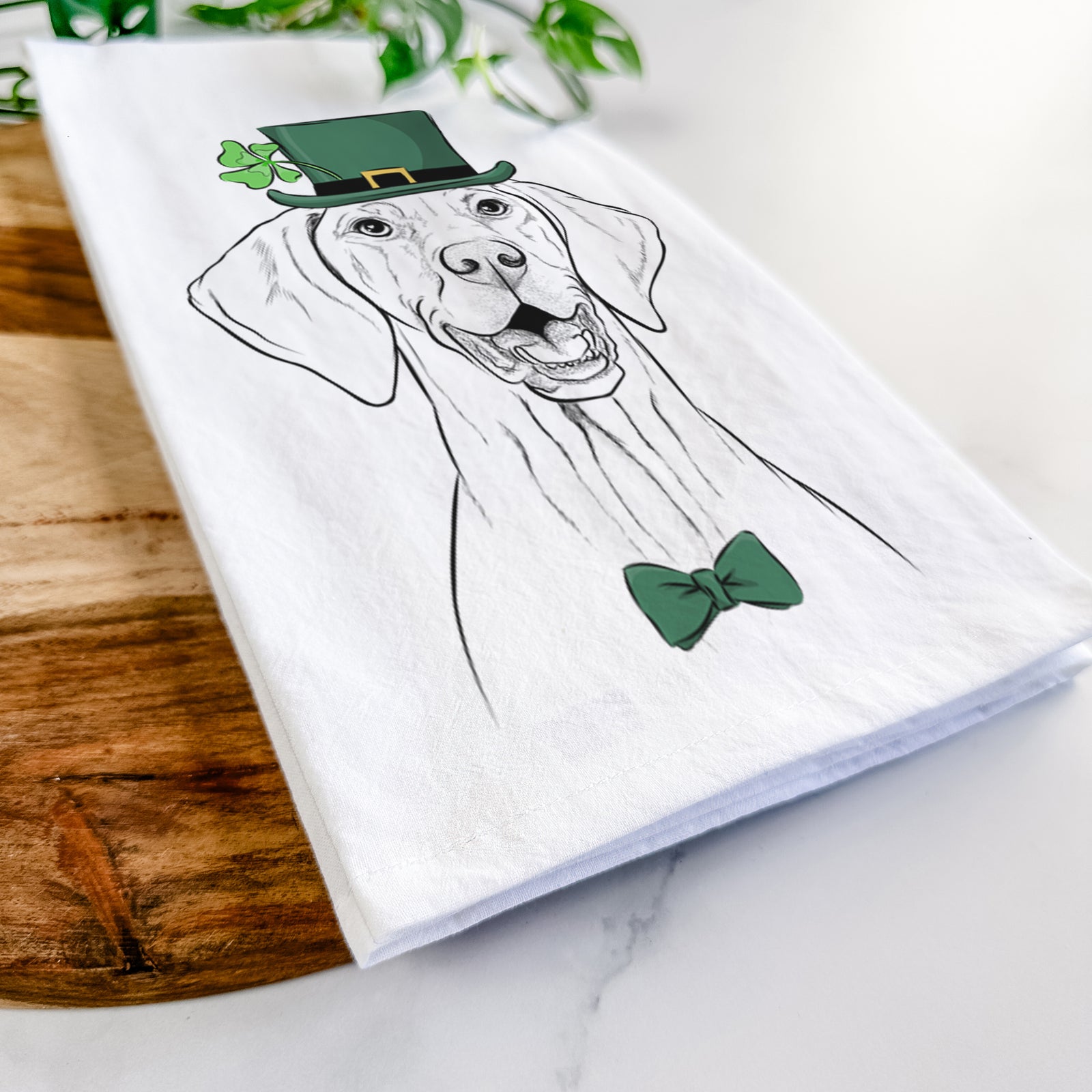 Hand-drawn sketch of Wesley the Vizsla wearing a St. Patrick's Day leprechaun hat and bow tie on a tea towel
