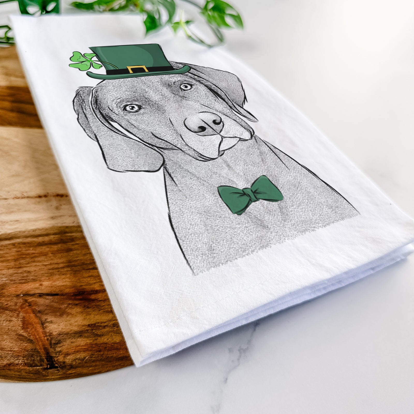 Hand-drawn sketch of Willow the Weizsla wearing a St. Patrick's Day leprechaun hat and bow tie on a tea towel