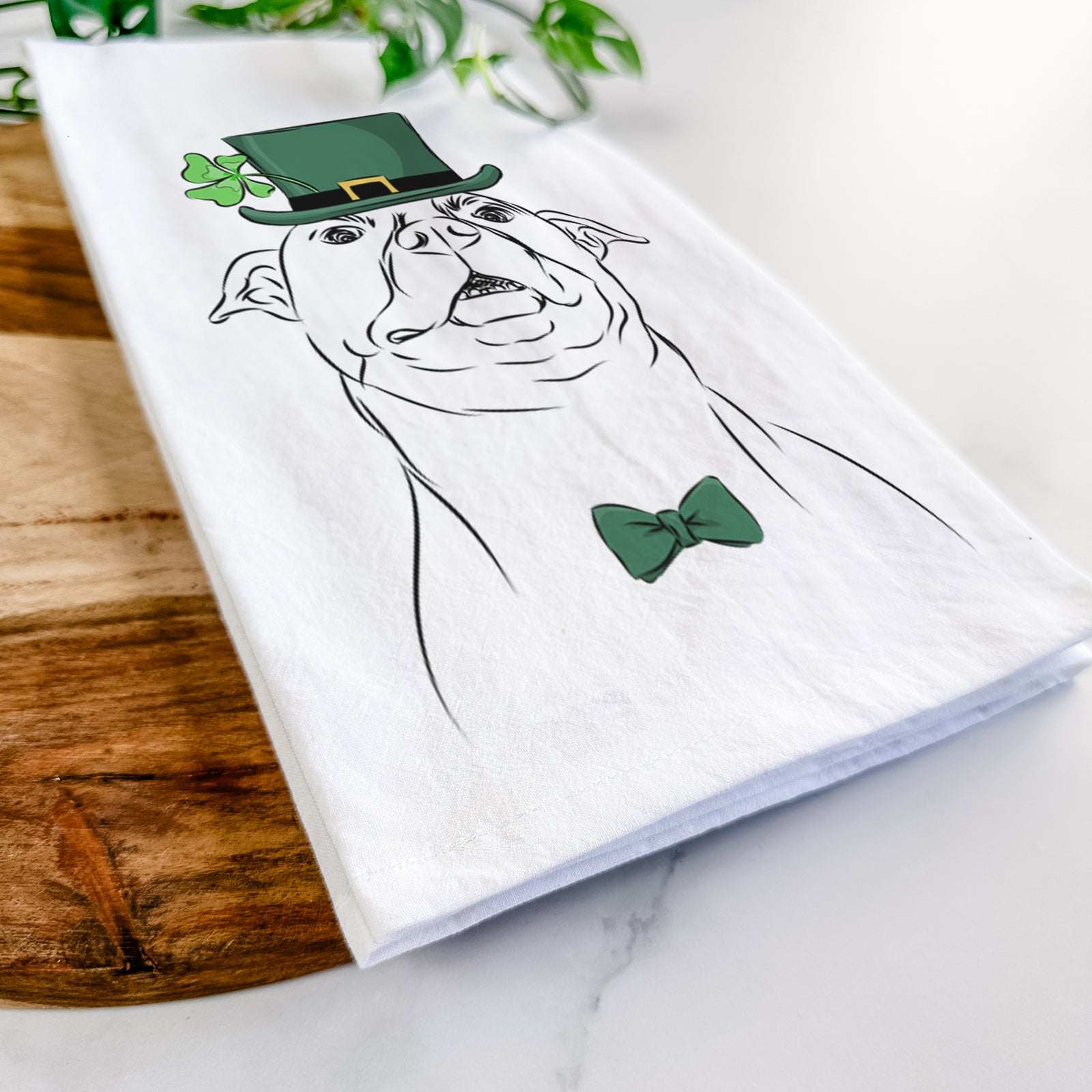 Hand-drawn sketch of Zada the Pitbull wearing a St. Patrick's Day leprechaun hat and bow tie on a tea towel