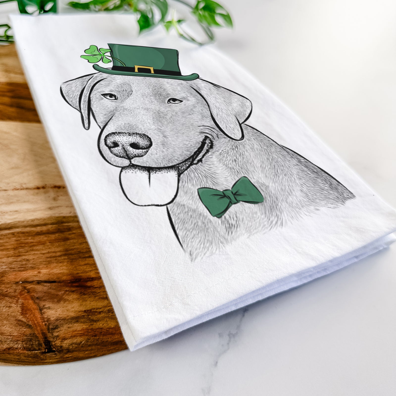 Hand-drawn sketch of Zeppelin the Black Labrador wearing a St. Patrick's Day leprechaun hat and bow tie on a tea towel