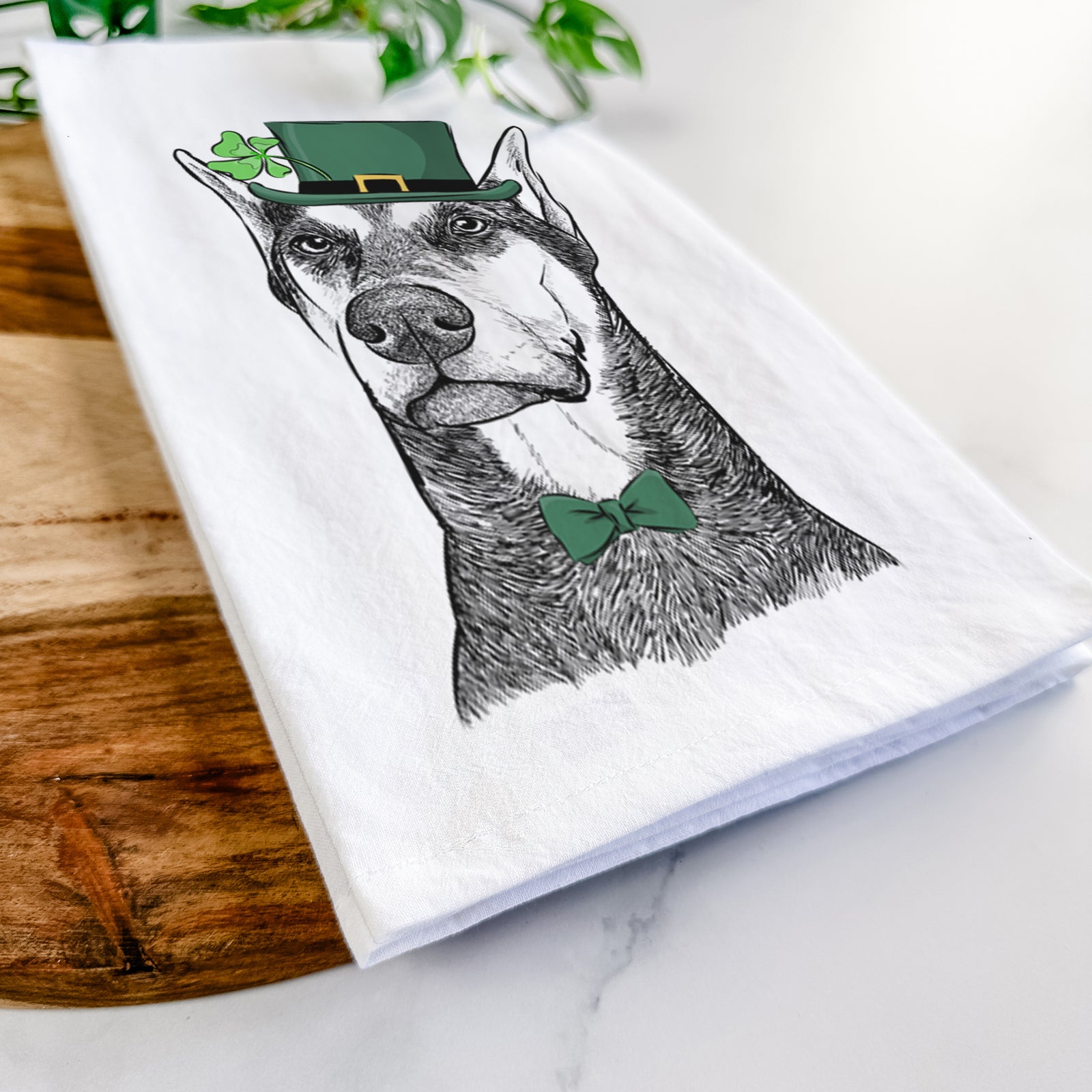 Hand-drawn sketch of Zeus the Doberman Pinscher wearing a St. Patrick's Day leprechaun hat and bow tie on a tea towel