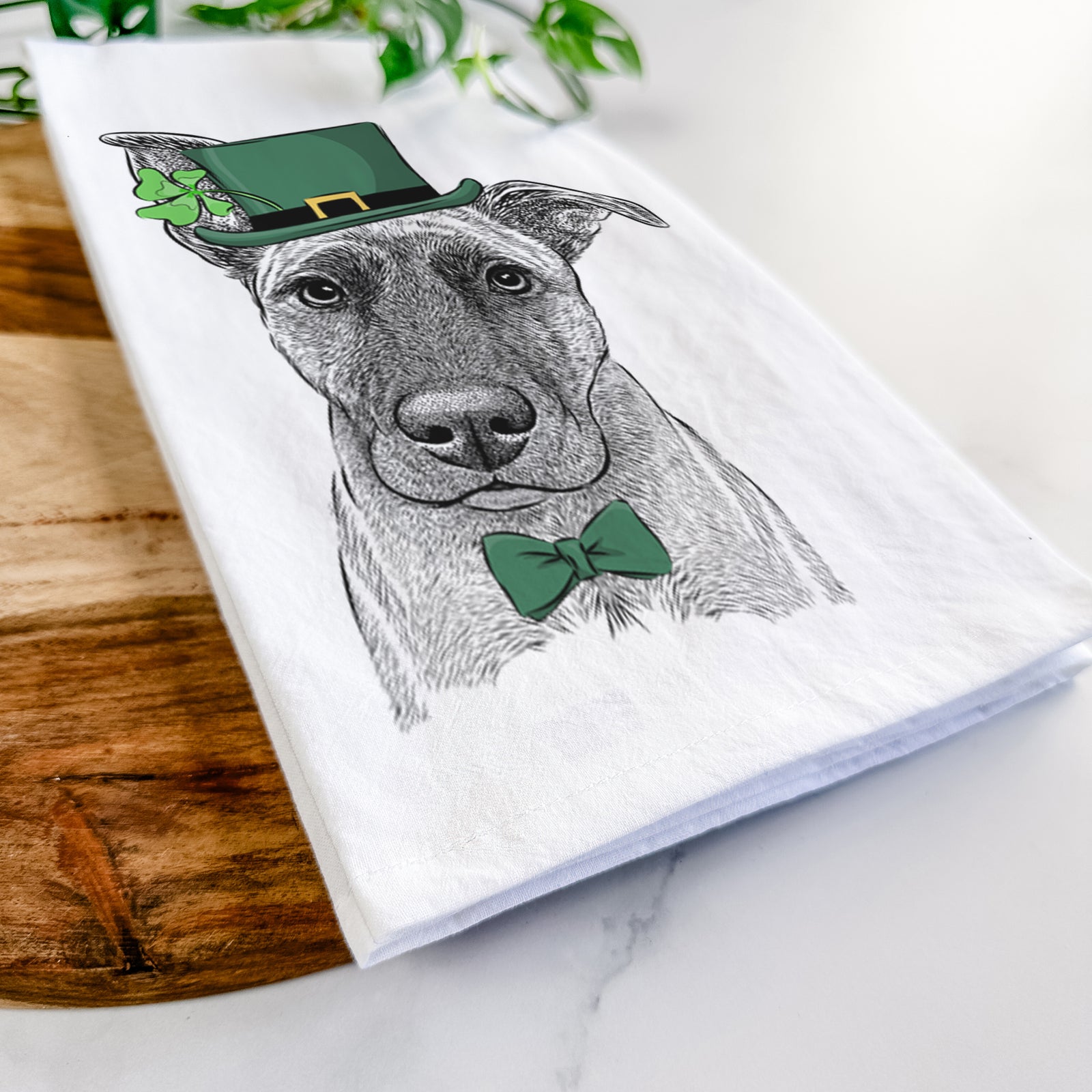 Hand-drawn sketch of Zoey the Mixed Breed wearing a St. Patrick's Day leprechaun hat and bow tie on a tea towel