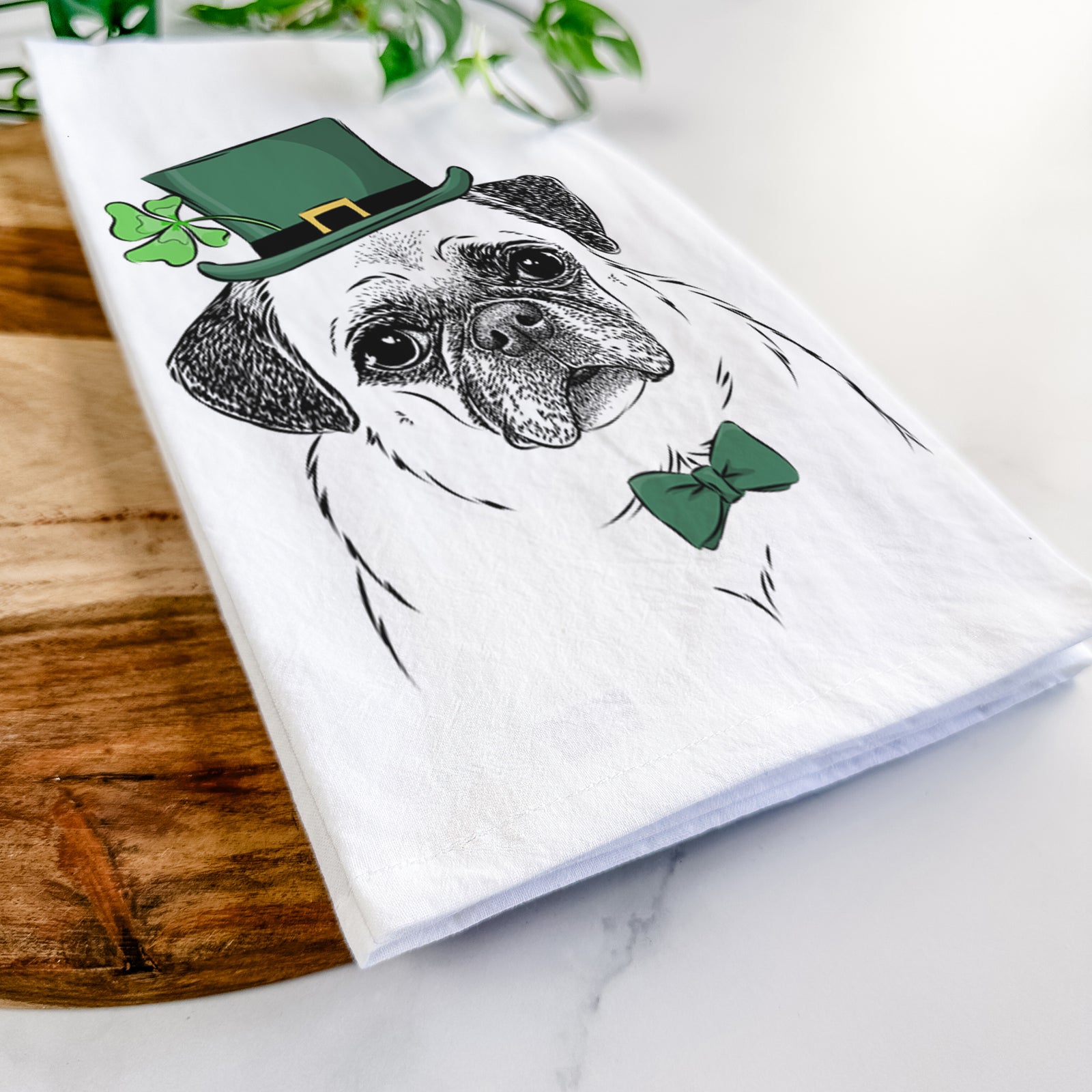 Hand-drawn sketch of Zoey the Pug wearing a St. Patrick's Day leprechaun hat and bow tie on a tea towel
