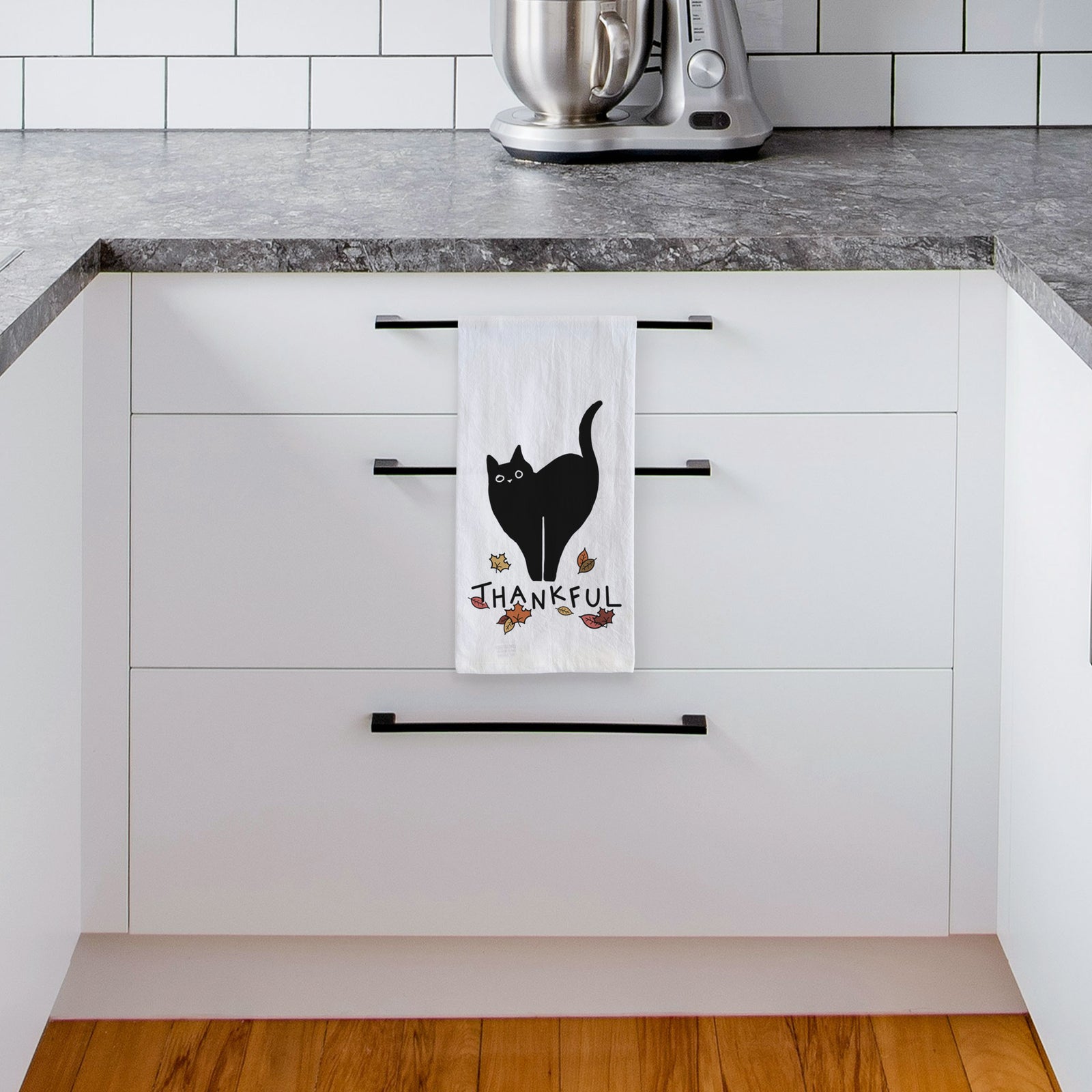 Minimalist line drawing of Bella the Black Cat with 'Thankful' lettering on a tea towel, hanging on an oven door in a kitchen