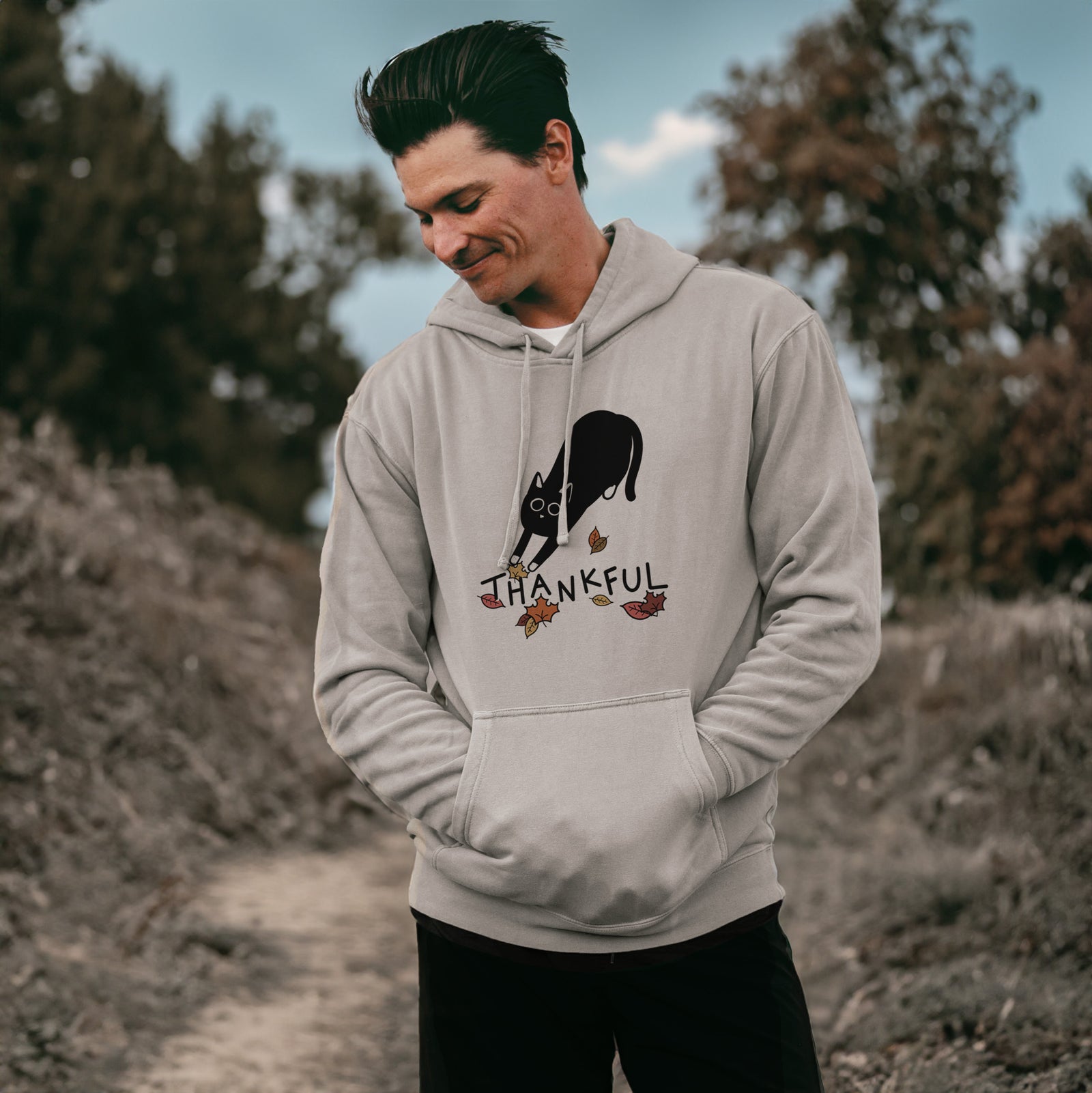 Minimalist line drawing of Bug the Black Cat with 'Thankful' lettering on a Cement Unisex pigment dyed hoodie, worn by a man