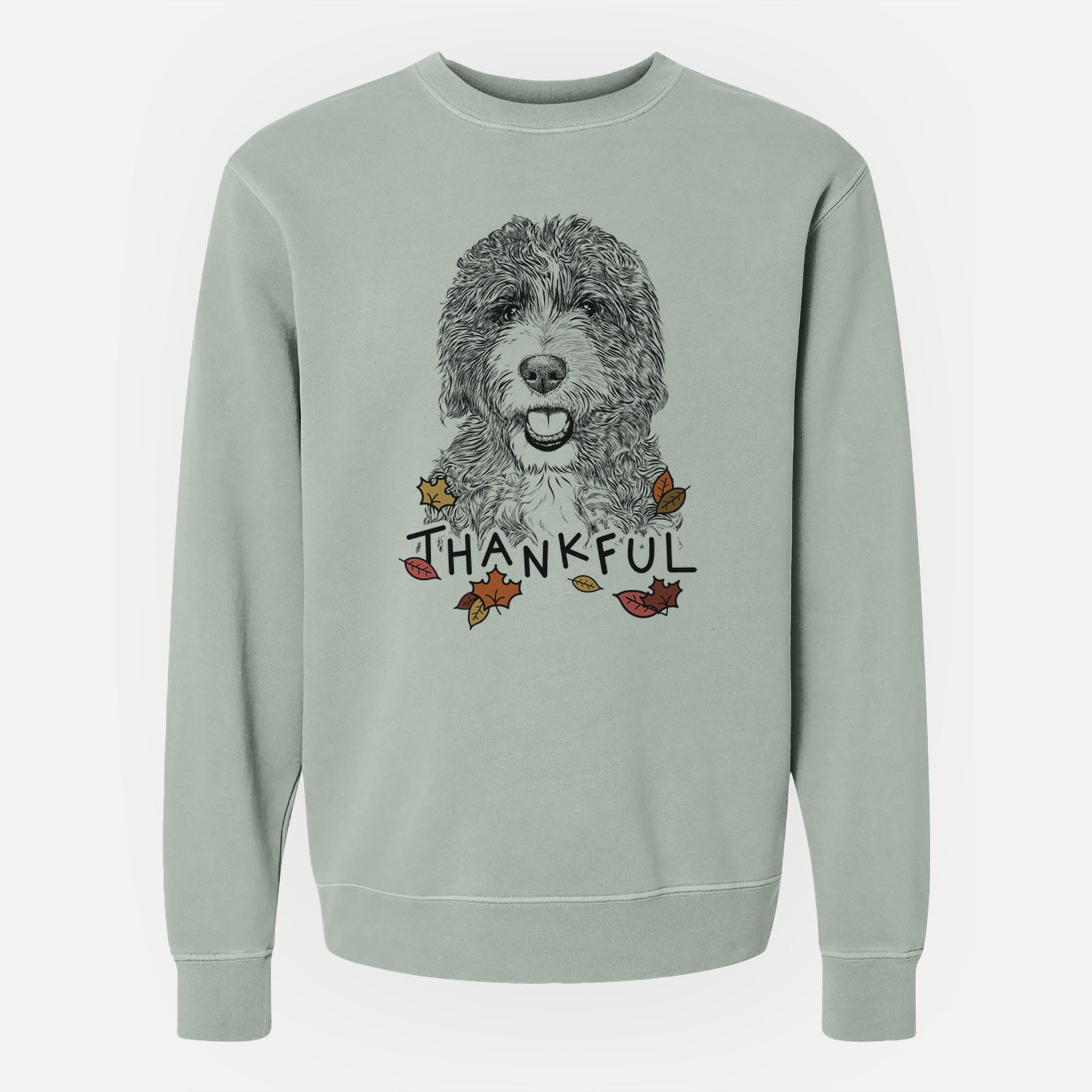 Hand-drawn sketch of Bash the Bernedoodle with 'Thankful' lettering and autumn leaves on a Sage Unisex pigment dyed crew sweatshirt