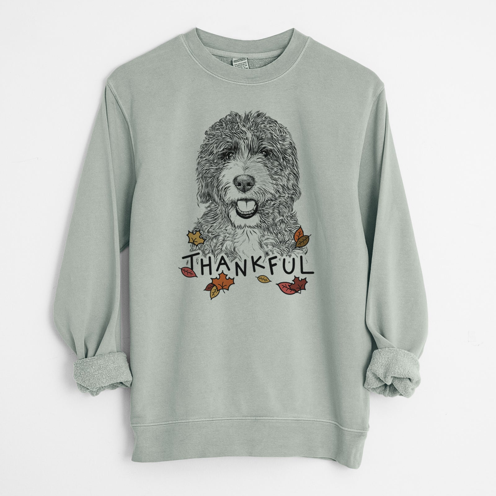 Hand-drawn sketch of Bash the Bernedoodle with 'Thankful' lettering and autumn leaves on a Sage Unisex pigment dyed crew sweatshirt