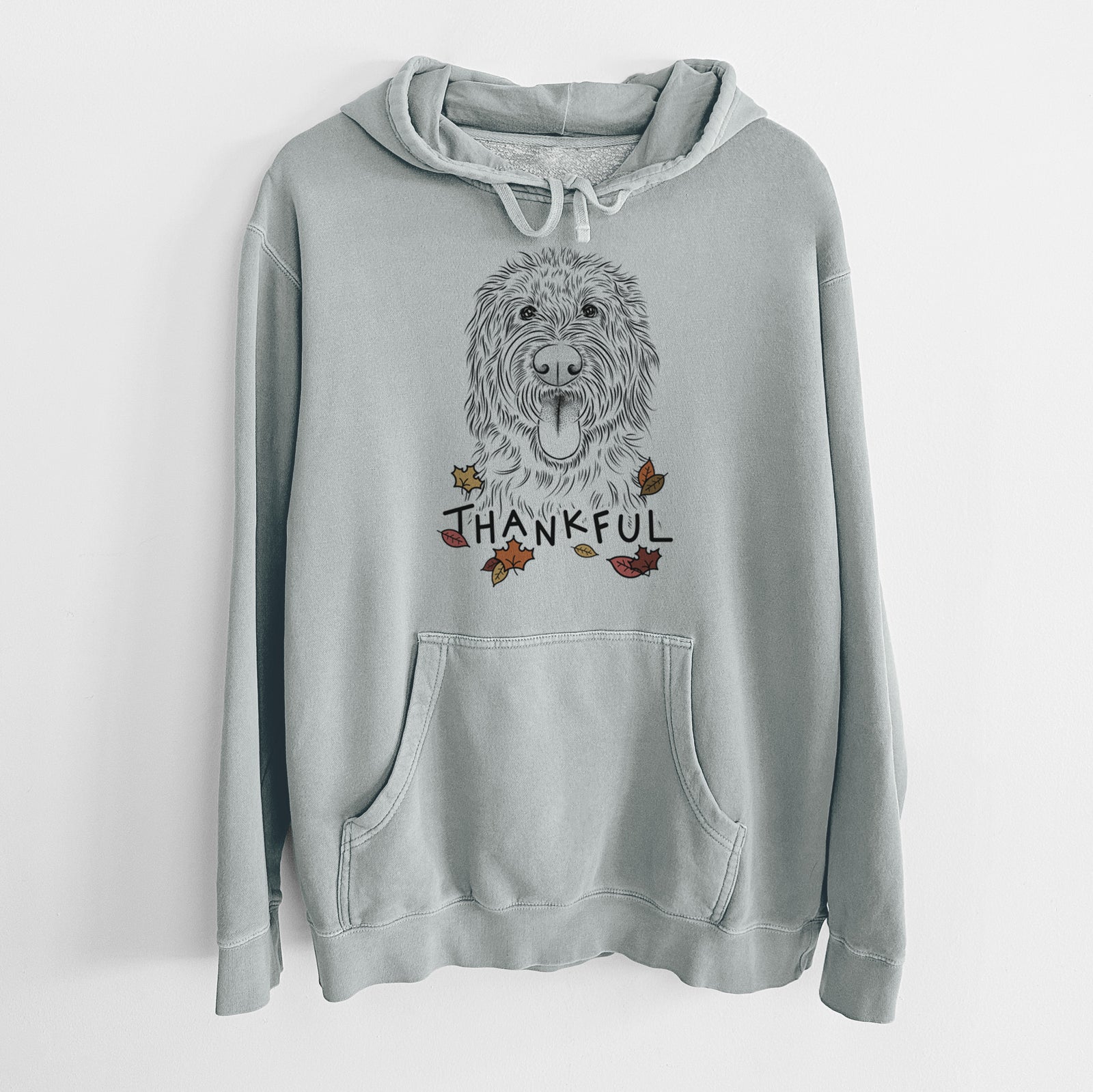 Hand-drawn sketch of Bennett the Doodle with 'Thankful' lettering and autumn leaves on a Sage Unisex pigment dyed hoodie
