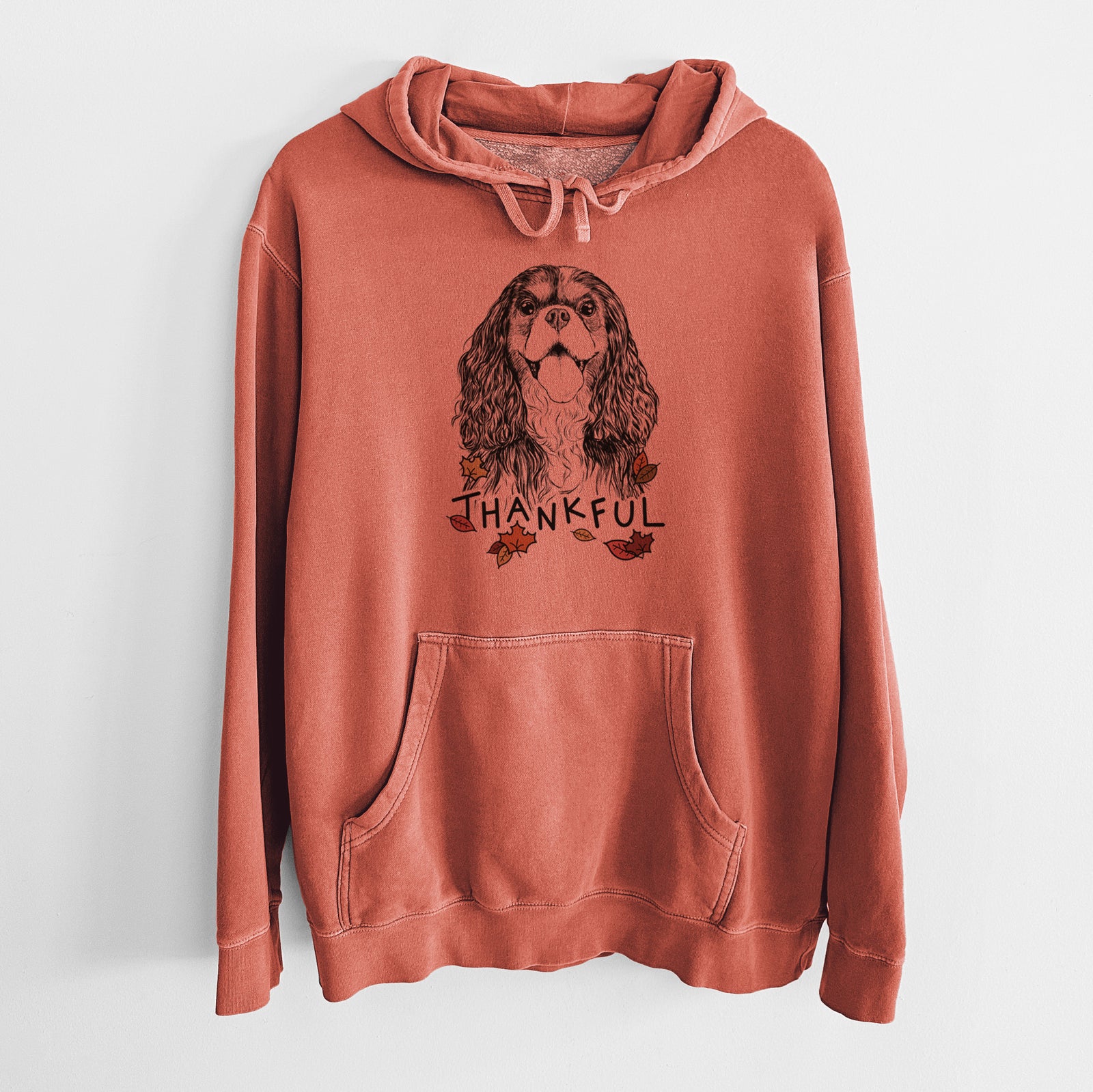 Hand-drawn sketch of Brandy the Cavalier King Charles Spaniel with 'Thankful' lettering and autumn leaves on an Amber Unisex pigment dyed hoodie