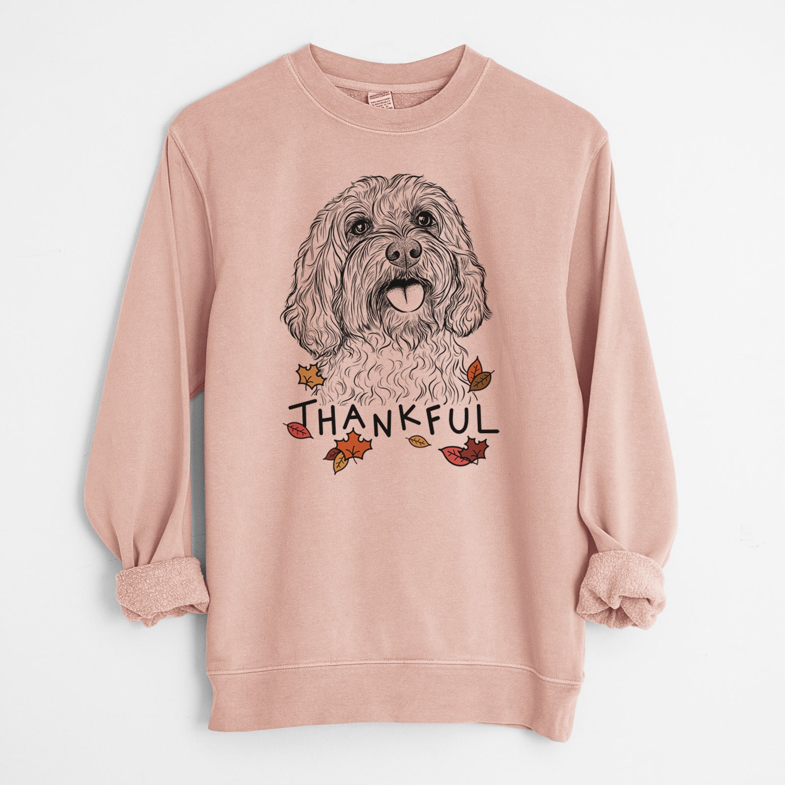 Hand-drawn sketch of Cali the Cavapoo with 'Thankful' lettering and autumn leaves on a Dusty Pink Unisex pigment dyed crew sweatshirt