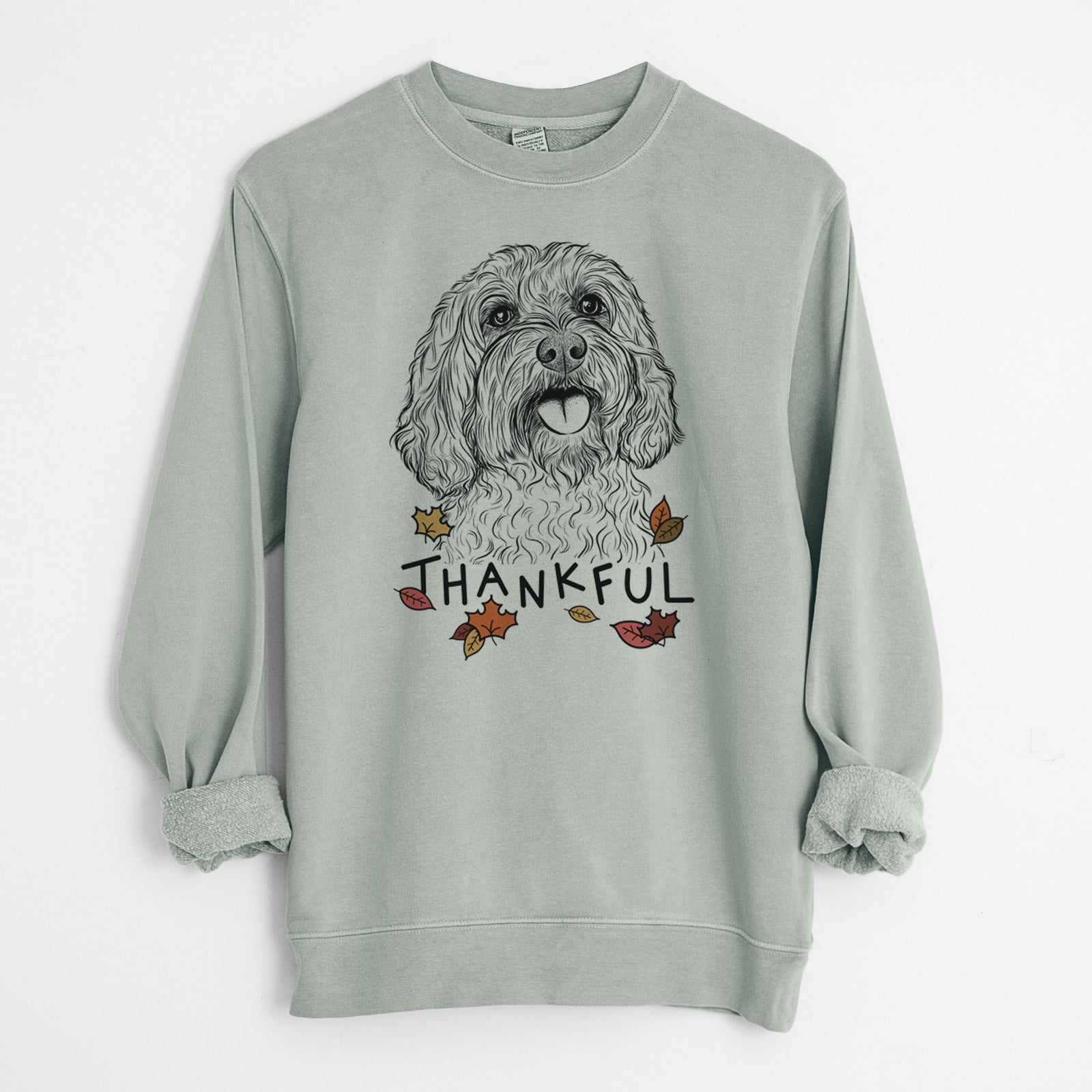 Hand-drawn sketch of Cali the Cavapoo with 'Thankful' lettering and autumn leaves on a Sage Unisex pigment dyed crew sweatshirt