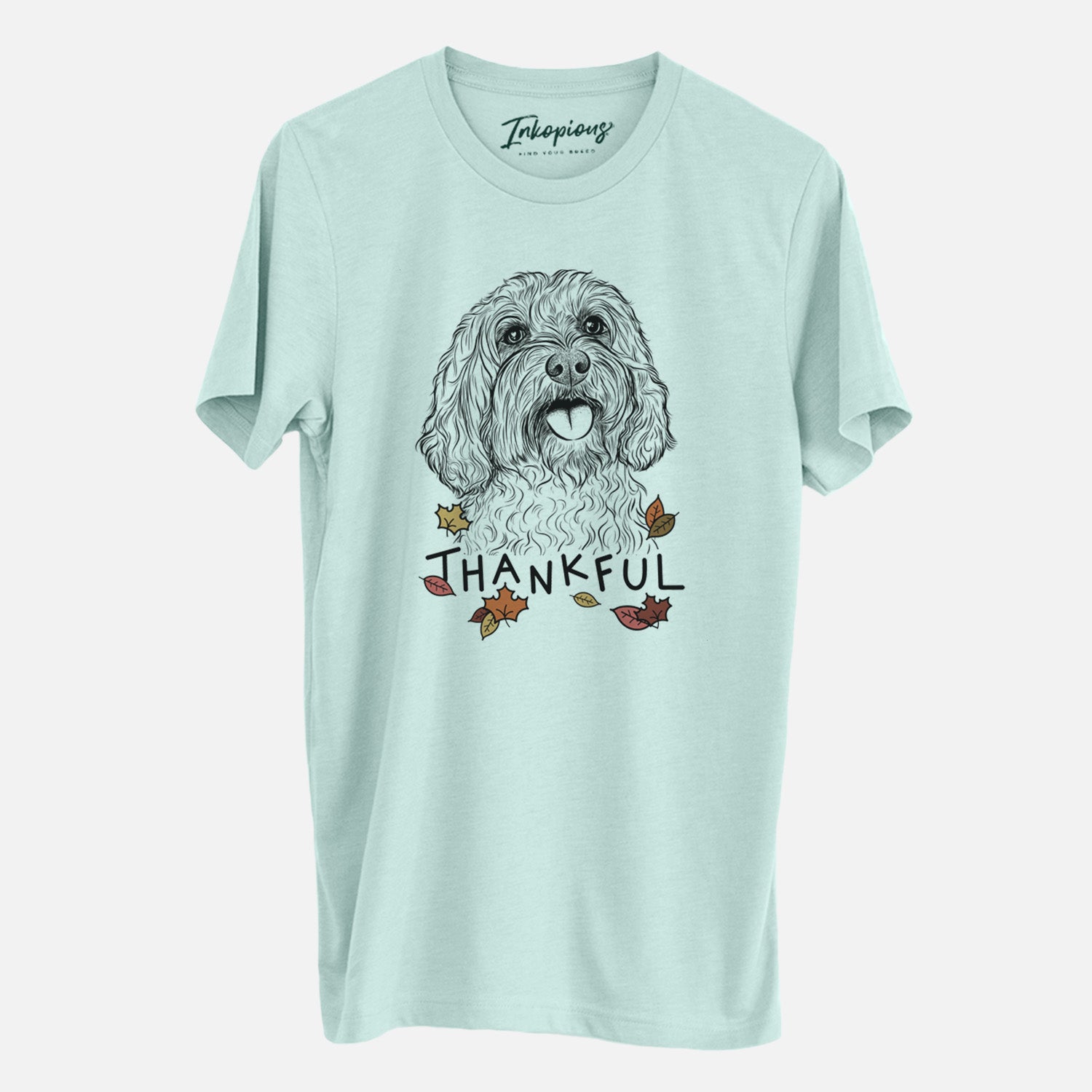Hand-drawn sketch of Cali the Cavapoo with 'Thankful' lettering and autumn leaves on a Heather Sage Unisex crewneck