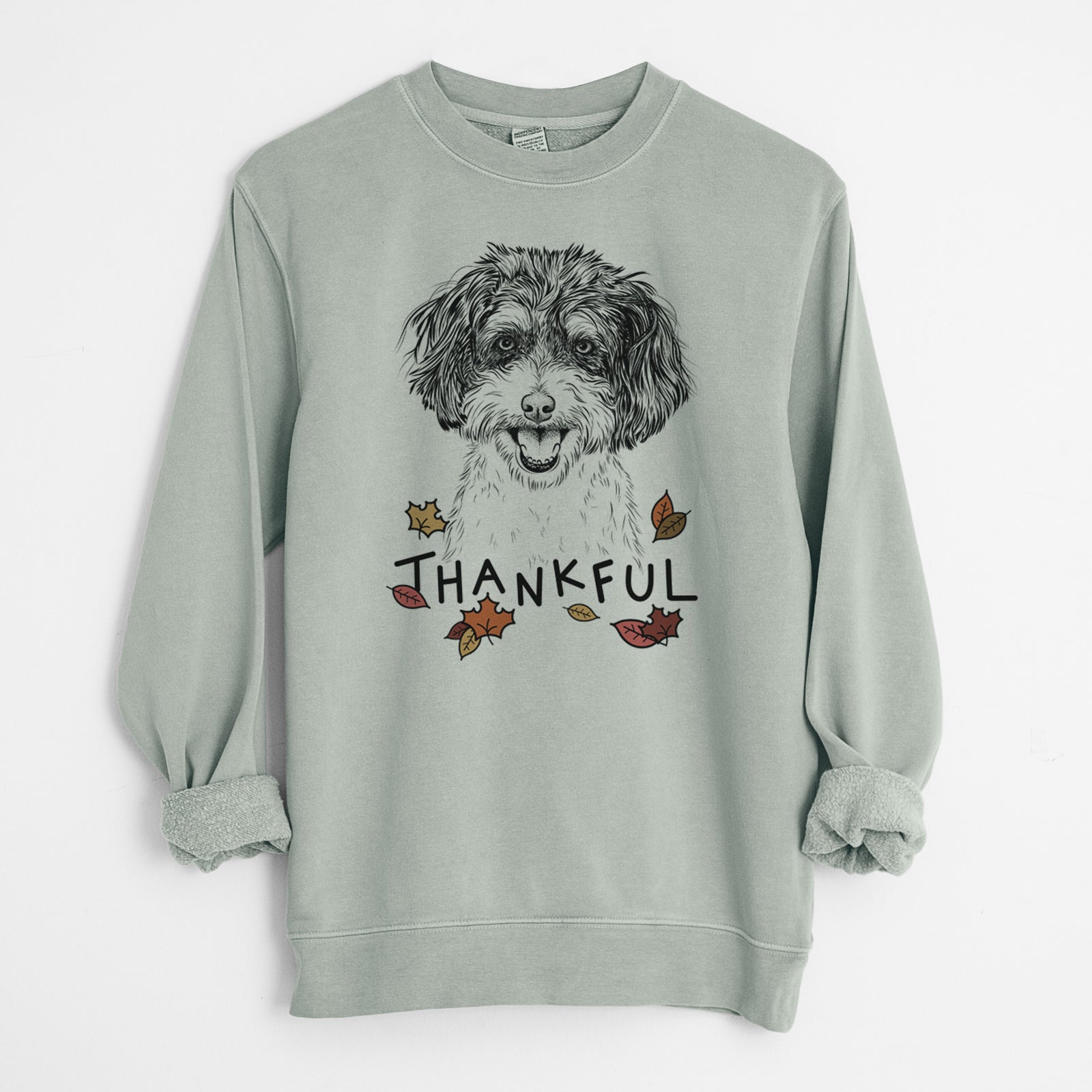 Hand-drawn sketch of Carlos the Cavapoo with 'Thankful' lettering and autumn leaves on a Sage Unisex pigment dyed crew sweatshirt