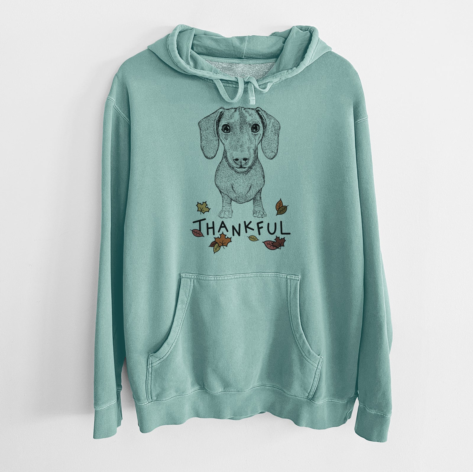 Hand-drawn sketch of Ernie the Mini Dachshund with 'Thankful' lettering and autumn leaves on a Mint Unisex pigment dyed hoodie