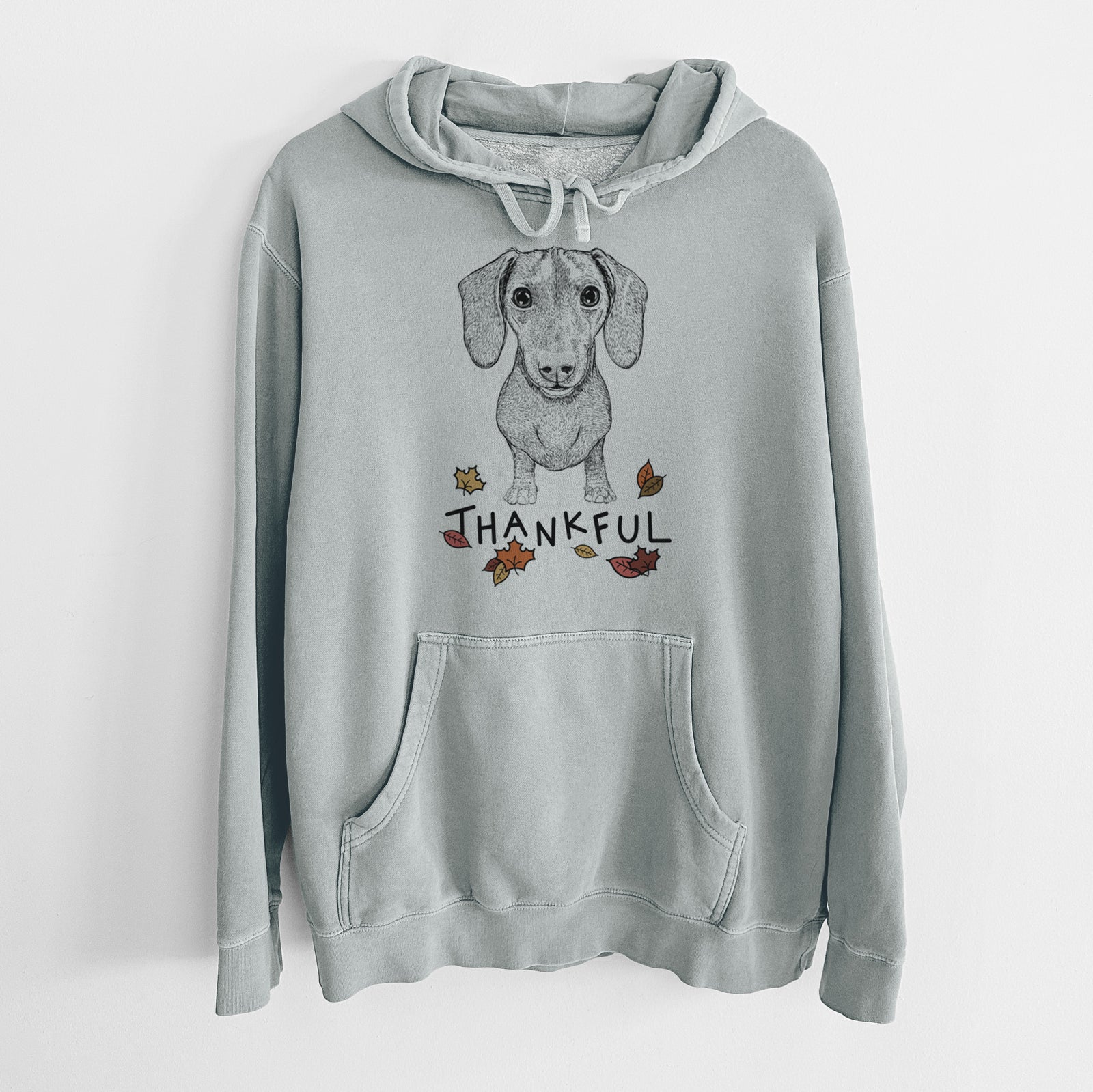 Hand-drawn sketch of Ernie the Mini Dachshund with 'Thankful' lettering and autumn leaves on a Sage Unisex pigment dyed hoodie