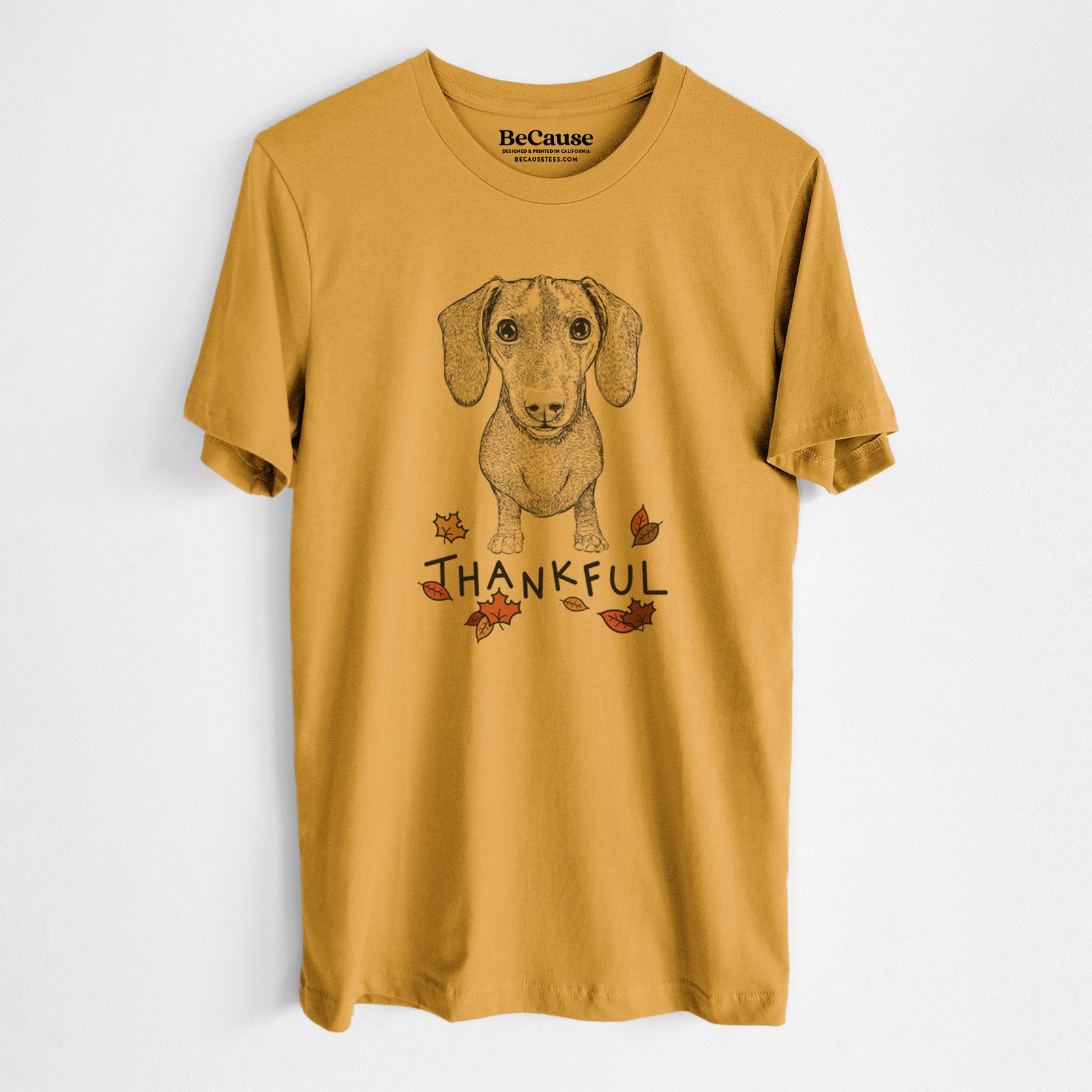 Hand-drawn sketch of Ernie the Mini Dachshund with 'Thankful' lettering and autumn leaves on a Mustard Unisex crewneck, worn by a man