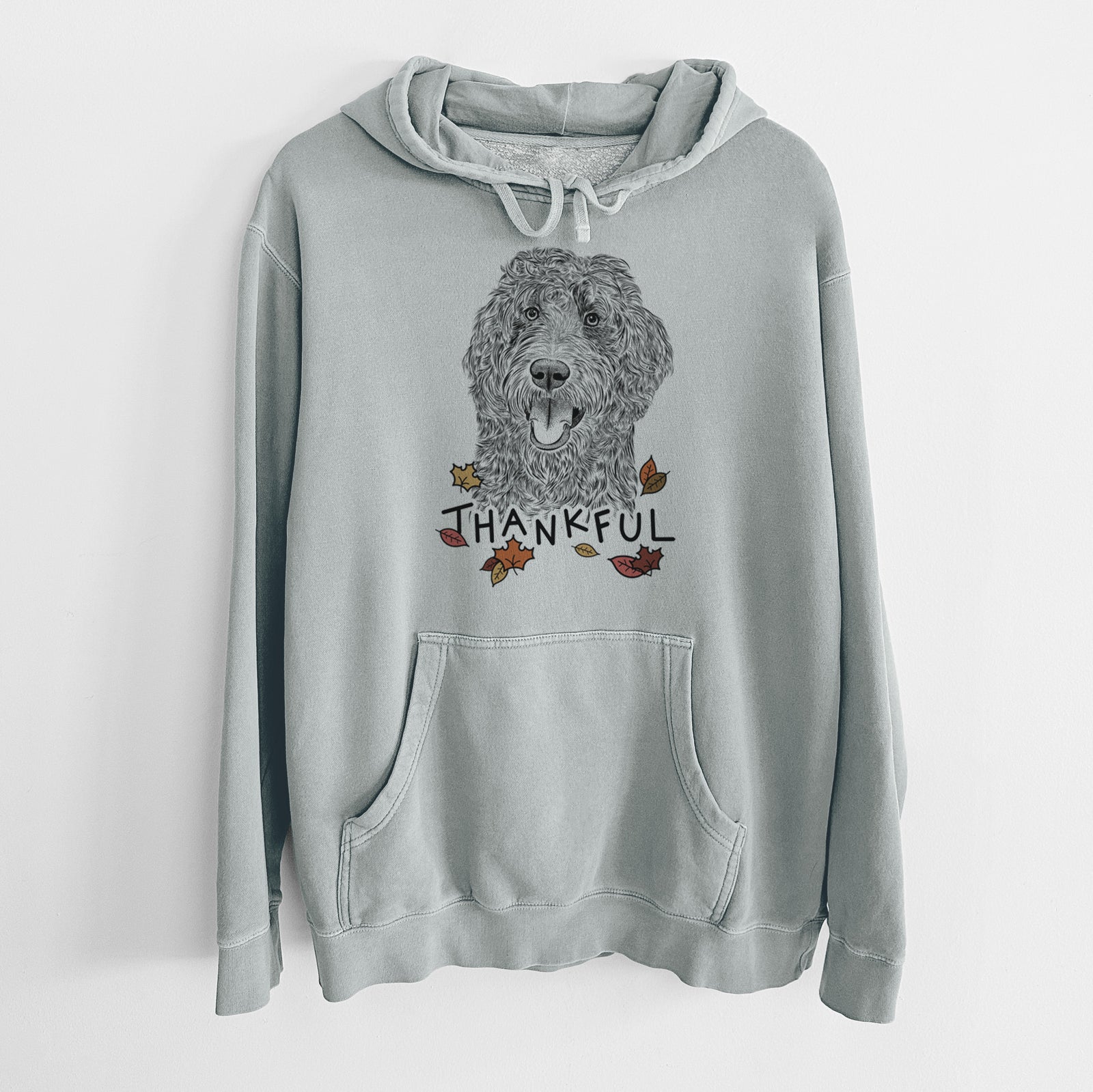 Hand-drawn sketch of Murr Dog the Labradoodle with 'Thankful' lettering and autumn leaves on a Sage Unisex pigment dyed hoodie