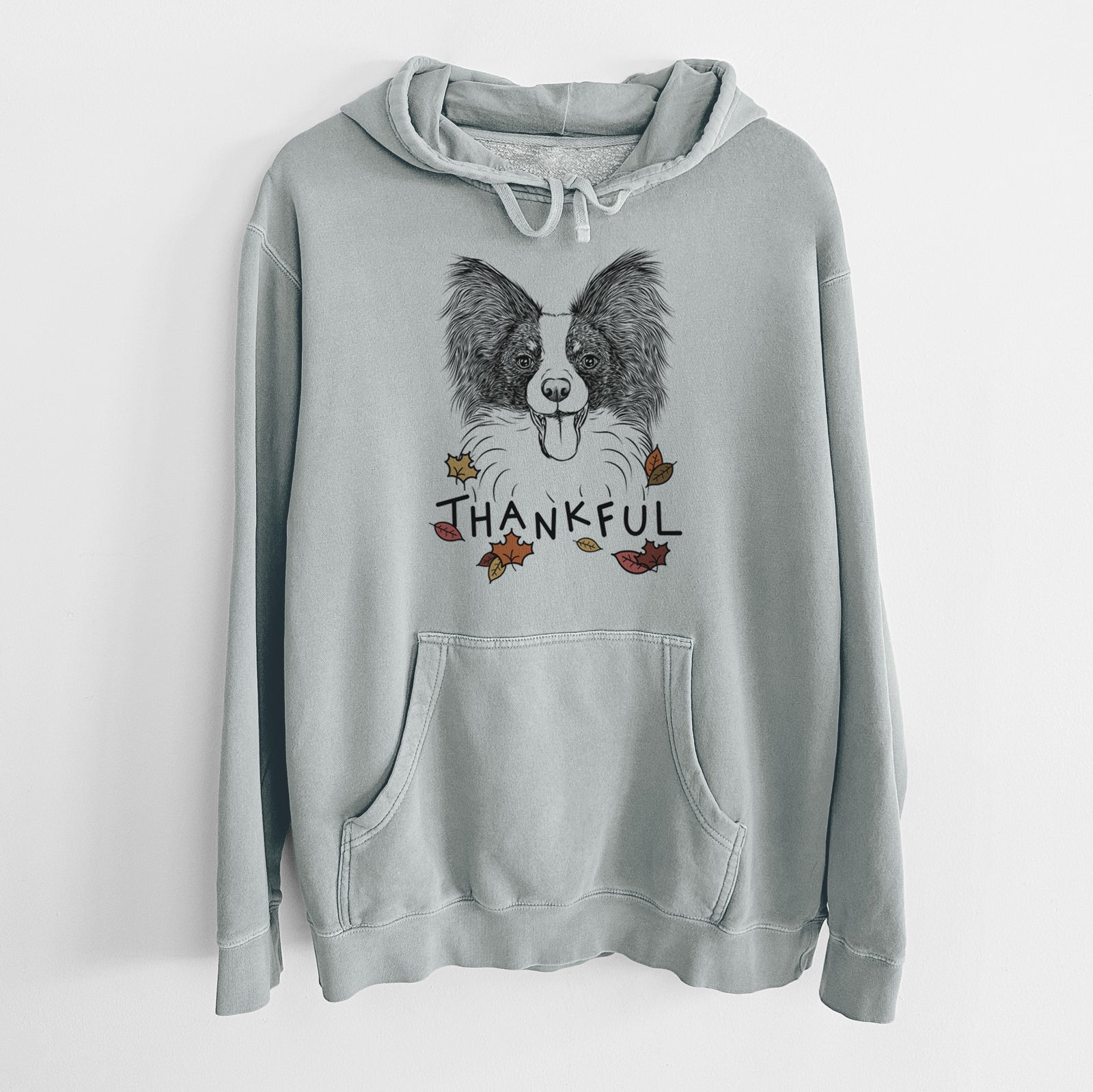 Hand-drawn sketch of Patrick the Papillon with 'Thankful' lettering and autumn leaves on a Sage Unisex pigment dyed hoodie