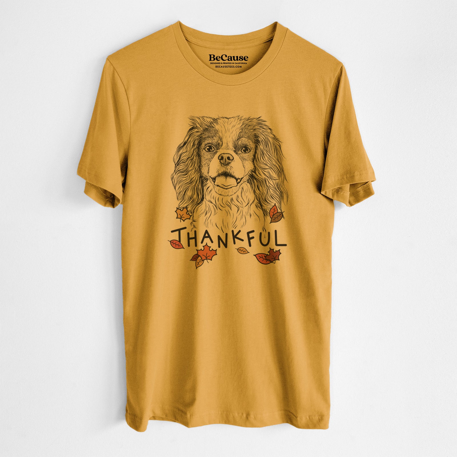 Hand-drawn sketch of Poppy the Cavalier King Charles Spaniel with 'Thankful' lettering and autumn leaves on a Mustard Unisex crewneck, worn by a man