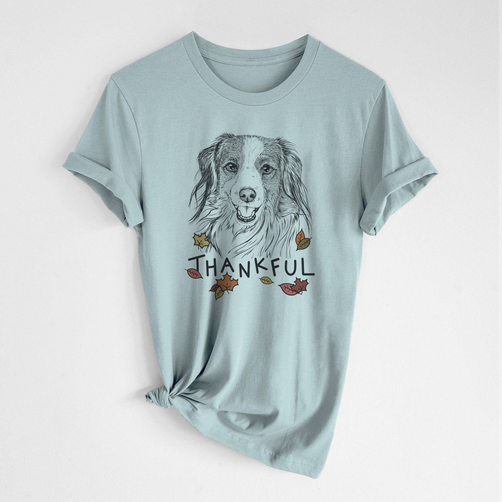 Hand-drawn sketch of Rutger the Nederlandse Kooikerhondje with 'Thankful' lettering and autumn leaves on a Dusty Blue Unisex crewneck, worn by a woman
