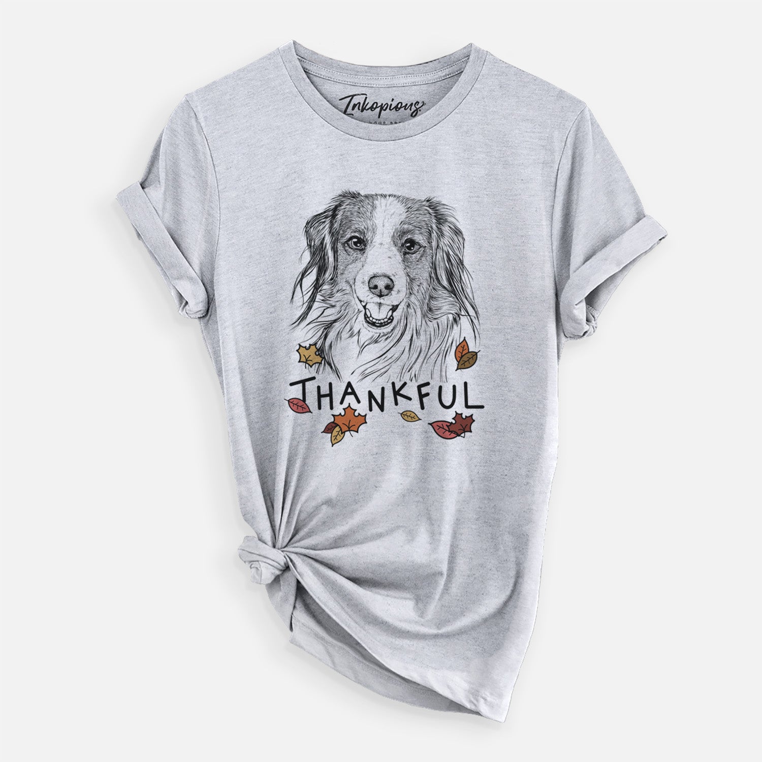 Hand-drawn sketch of Rutger the Nederlandse Kooikerhondje with 'Thankful' lettering and autumn leaves on a Grey Unisex crewneck, worn by a woman