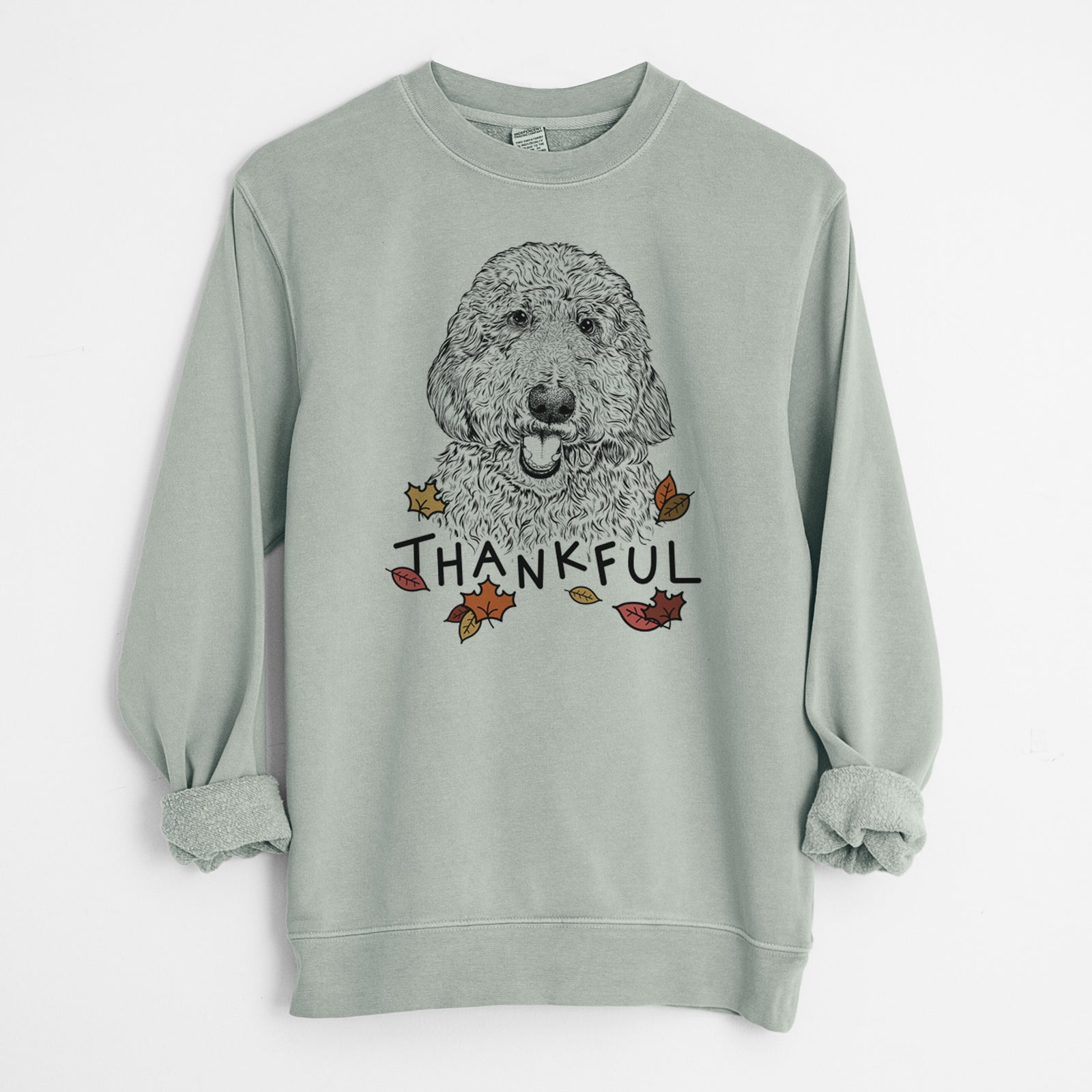 Hand-drawn sketch of Whisper the Goldendoodle with 'Thankful' lettering and autumn leaves on a Sage Unisex pigment dyed crew sweatshirt