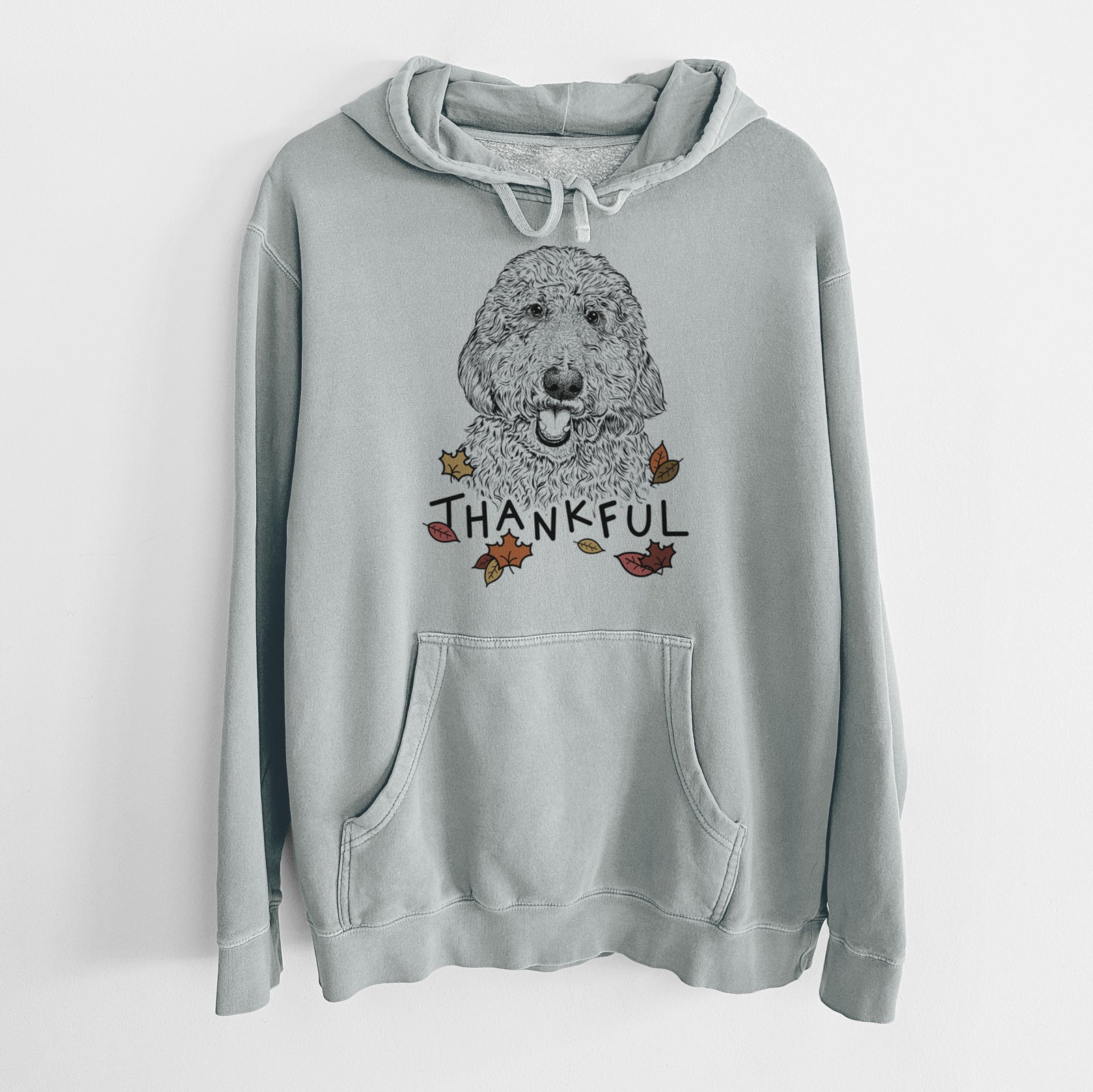 Hand-drawn sketch of Whisper the Goldendoodle with 'Thankful' lettering and autumn leaves on a Sage Unisex pigment dyed hoodie