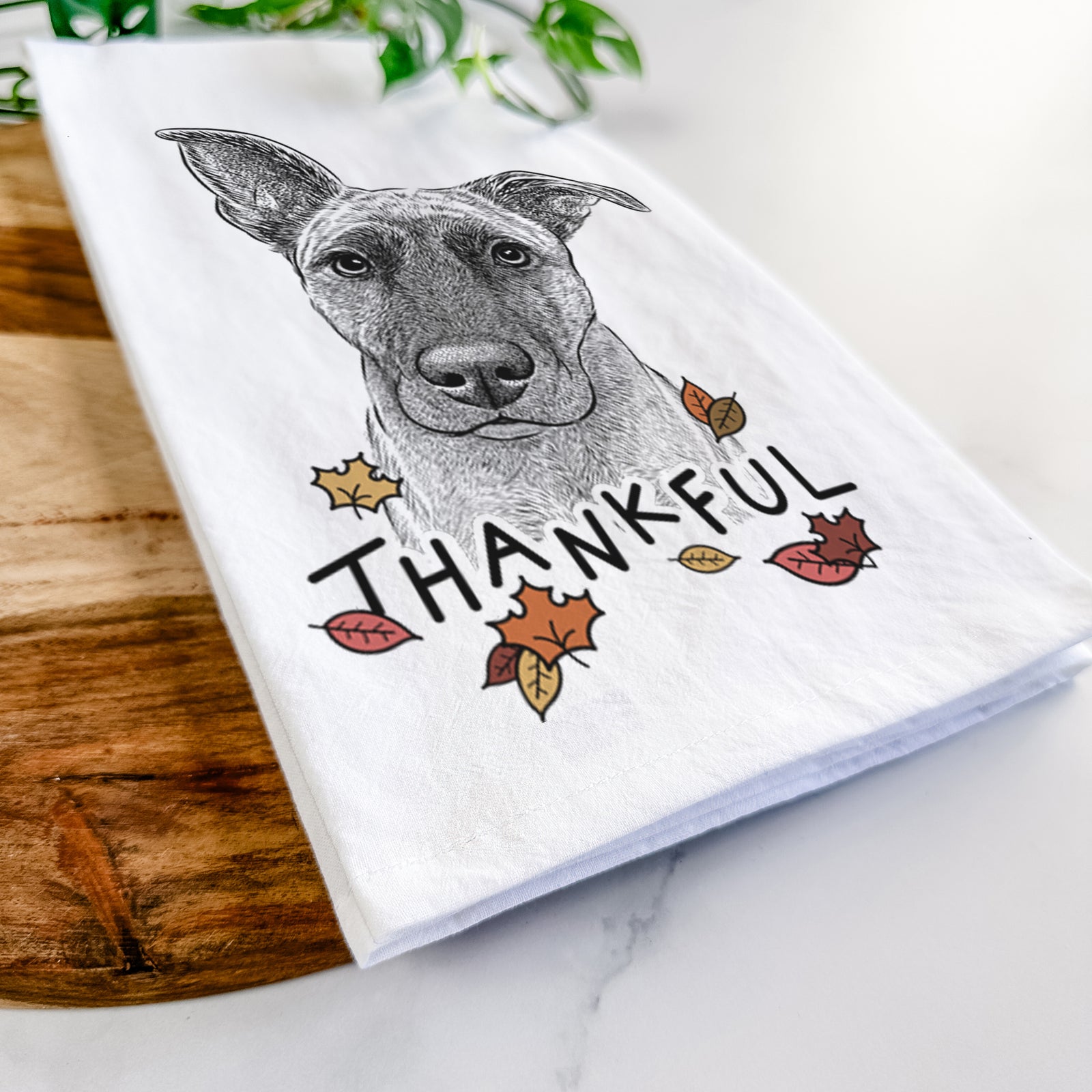Hand-drawn sketch of Zoey the Mixed Breed with 'Thankful' lettering and autumn leaves on a tea towel