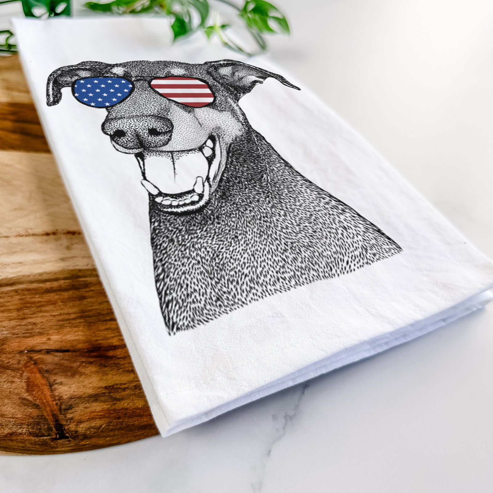 Hand-drawn sketch of Bunnie the Doberman Pinscher wearing American flag sunglasses on a tea towel