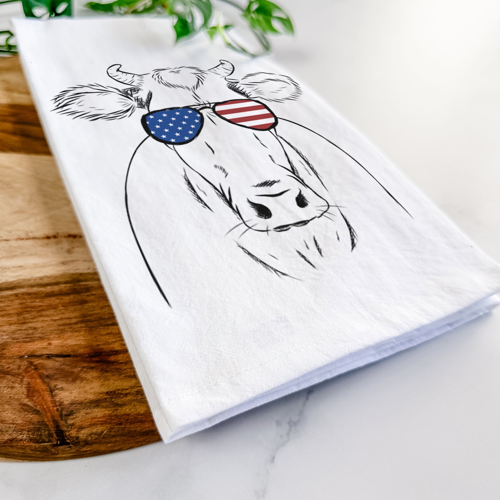 Hand-drawn sketch of Cruz the Cow wearing American flag sunglasses on a tea towel