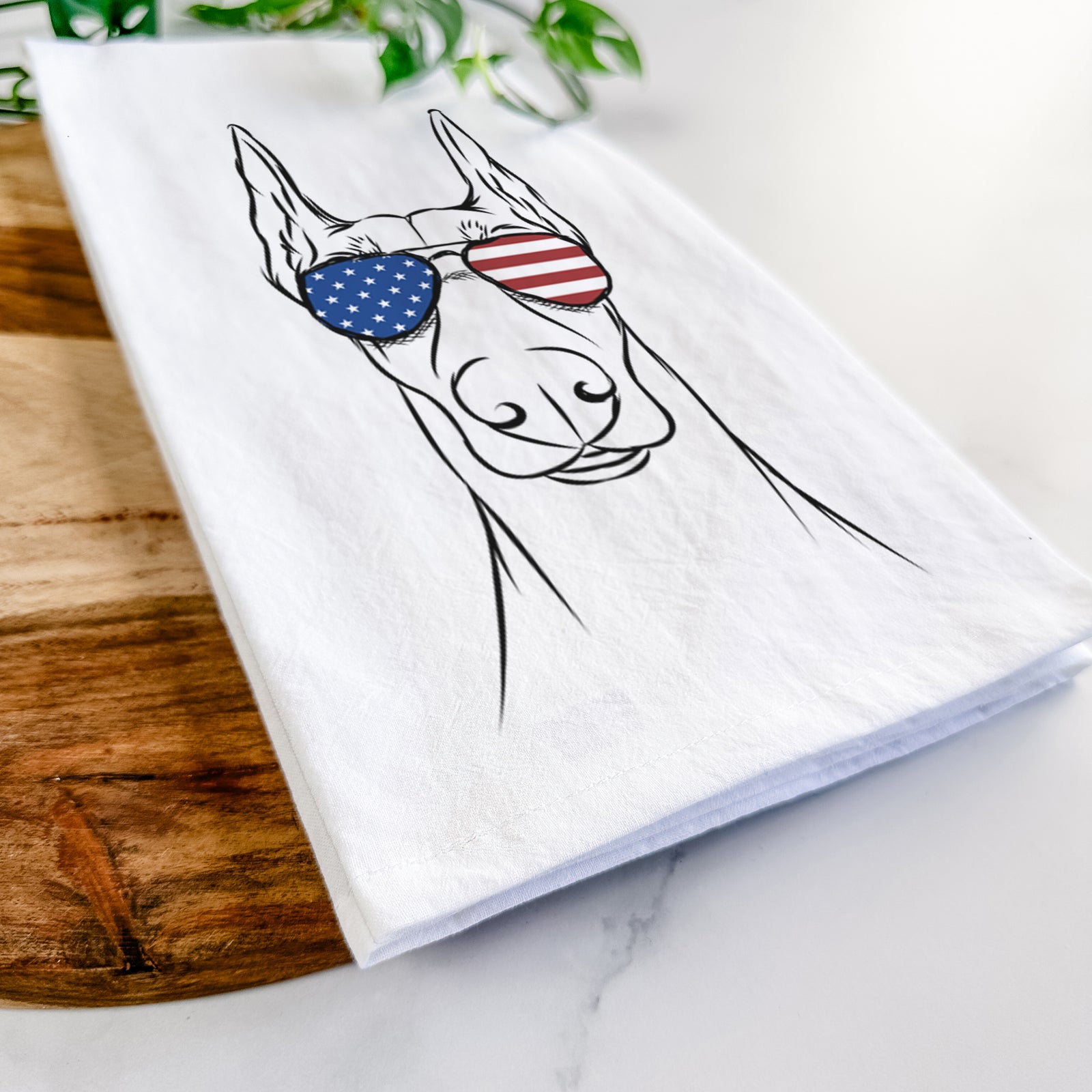 Hand-drawn sketch of Duke the Doberman Pinscher wearing American flag sunglasses on a tea towel