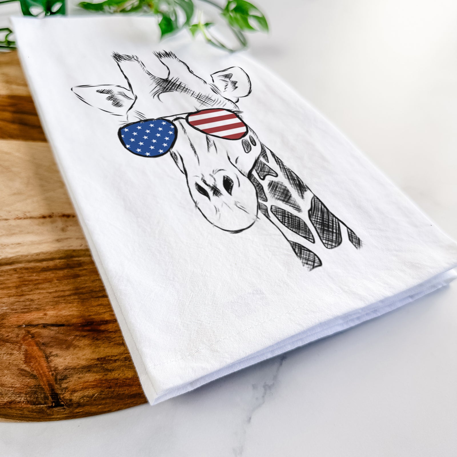 Hand-drawn sketch of Geoffrey the Giraffe wearing American flag sunglasses on a tea towel