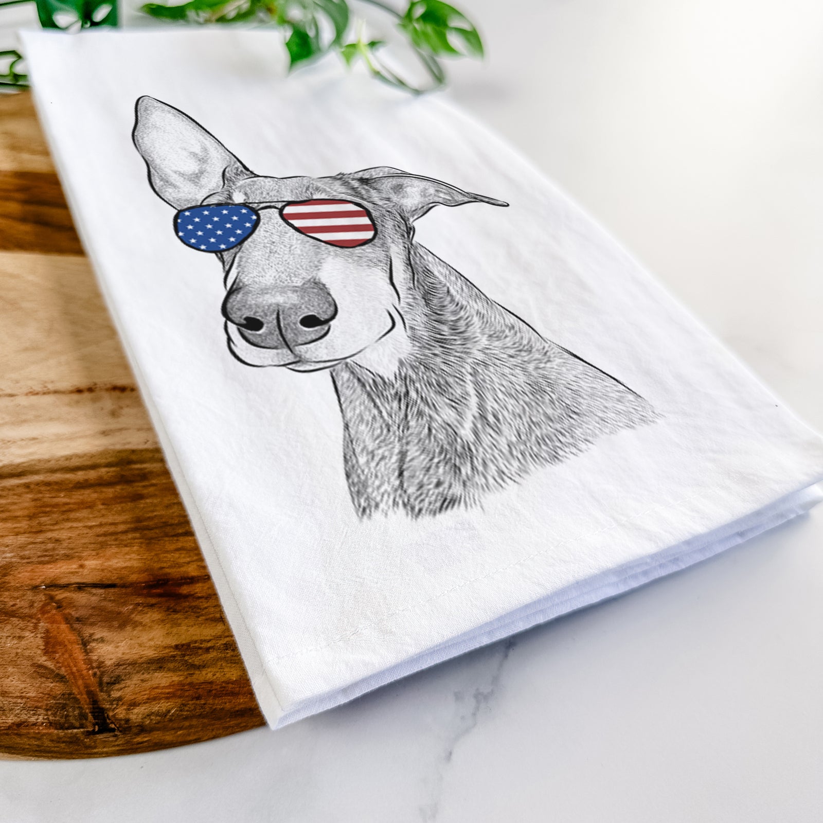 Hand-drawn sketch of Kain the Doberman Pinscher wearing American flag sunglasses on a tea towel