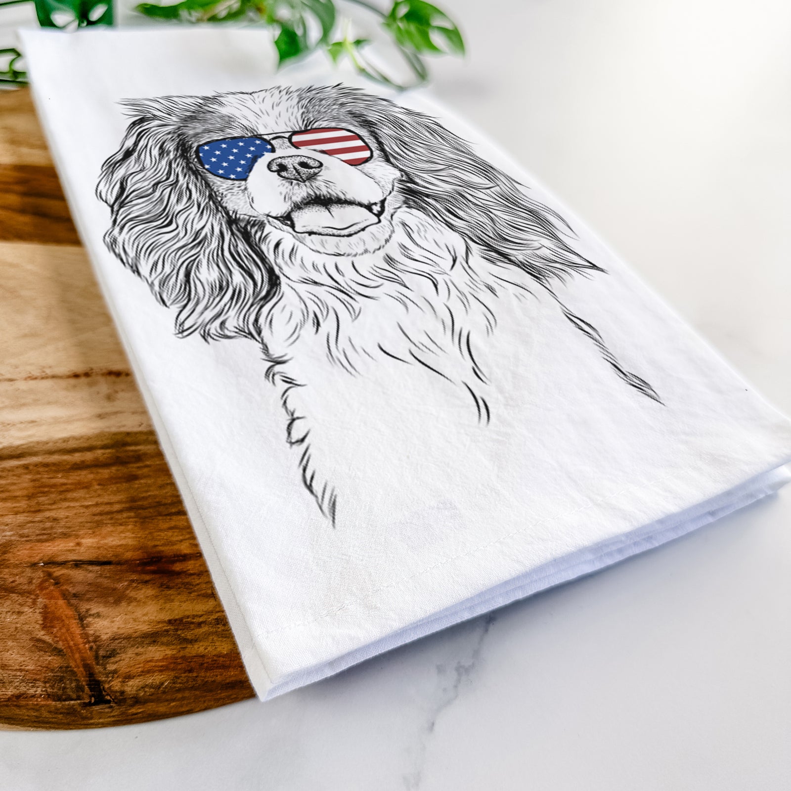 Hand-drawn sketch of Poppy the Cavalier King Charles Spaniel wearing American flag sunglasses on a tea towel