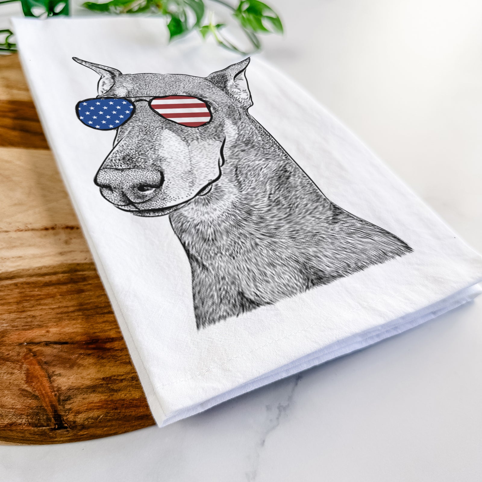 Hand-drawn sketch of Shelby the Doberman Pinscher wearing American flag sunglasses on a tea towel