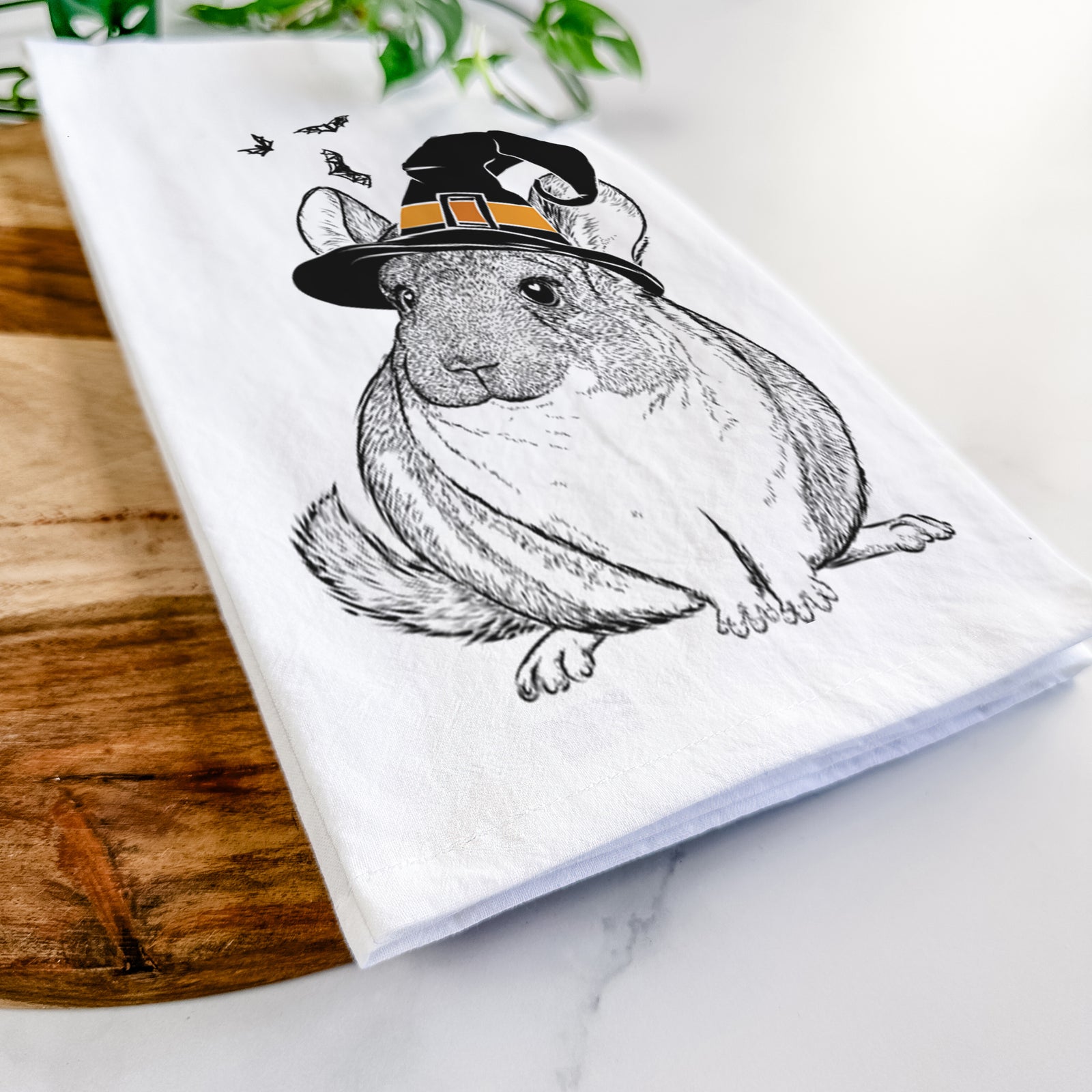 Hand-drawn sketch of Cheddar the Chinchilla wearing a witch hat on a tea towel